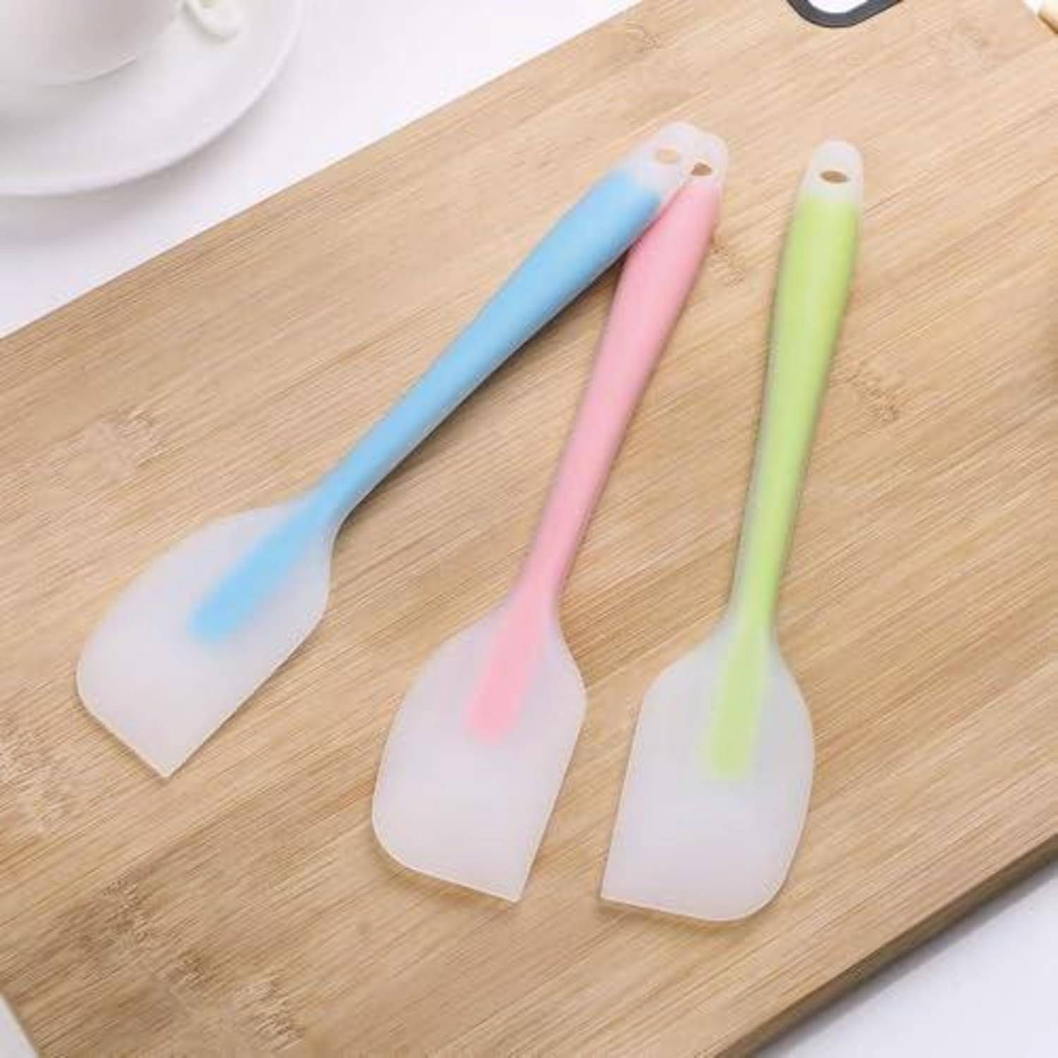 Drei Silikonspachteln mit blauen, rosa und grünen Griffen liegen auf einem Holzschneidebrett.