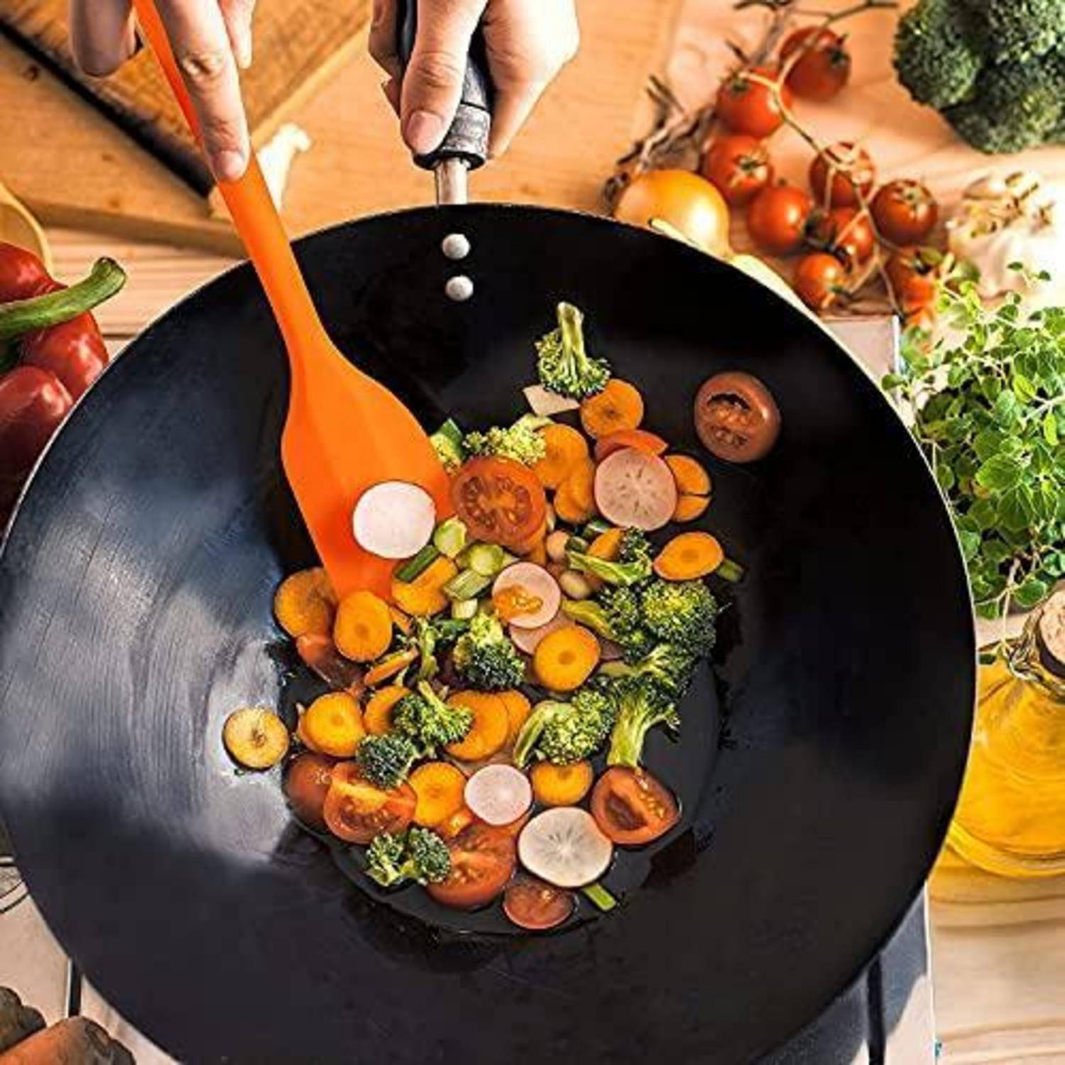 Hände braten gemischtes Gemüse in einem schwarzen Wok mit einem orangefarbenen Spatula um, umgeben von frischen Produkten auf einer hölzernen Arbeitsplatte.