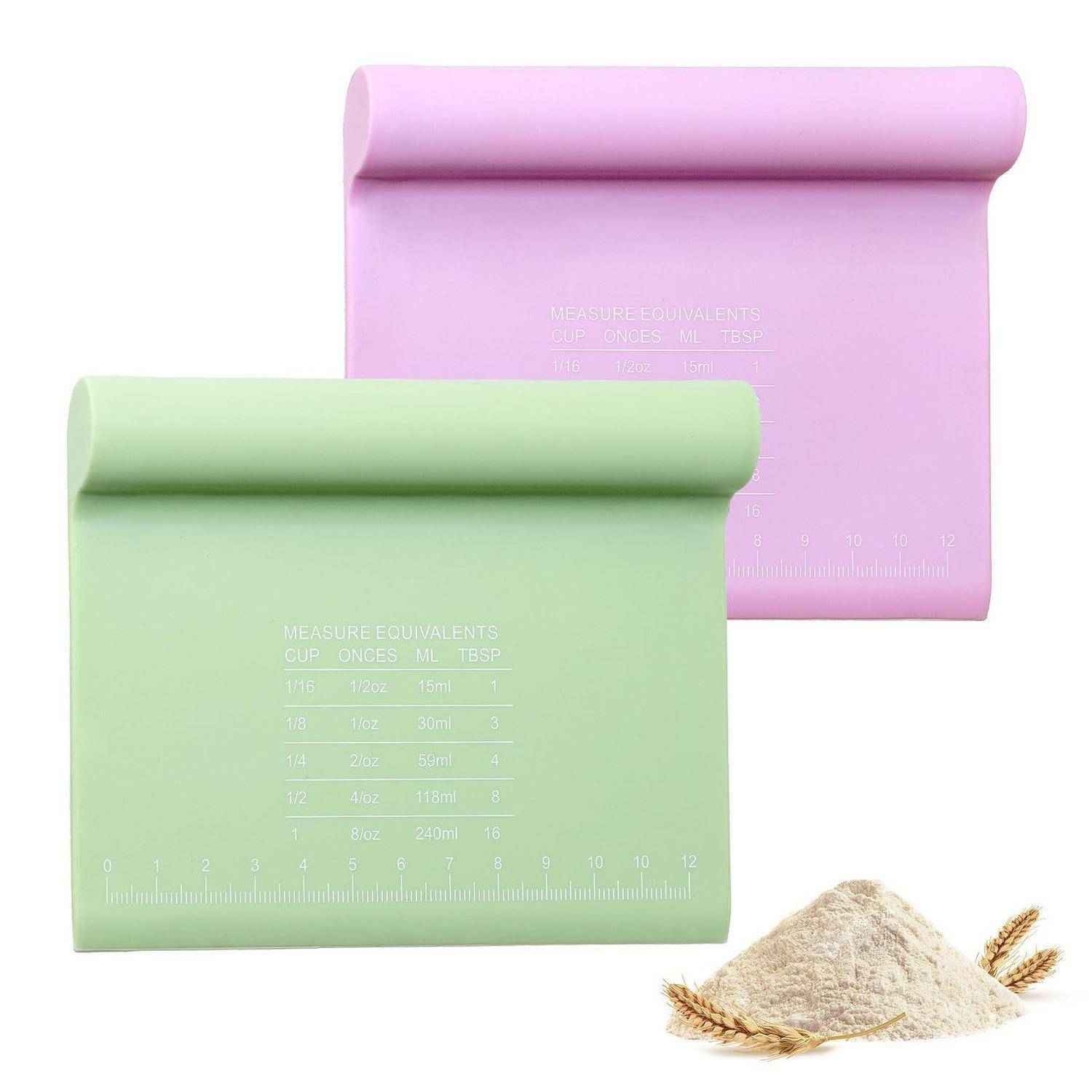 Zwei Pastellmessmatten, grün und rosa, mit gedruckten Umrechnungen für Tassen/Unzen/mL/Esslöffel, plus ein kleiner Haufen Mehl und Weizenähren.