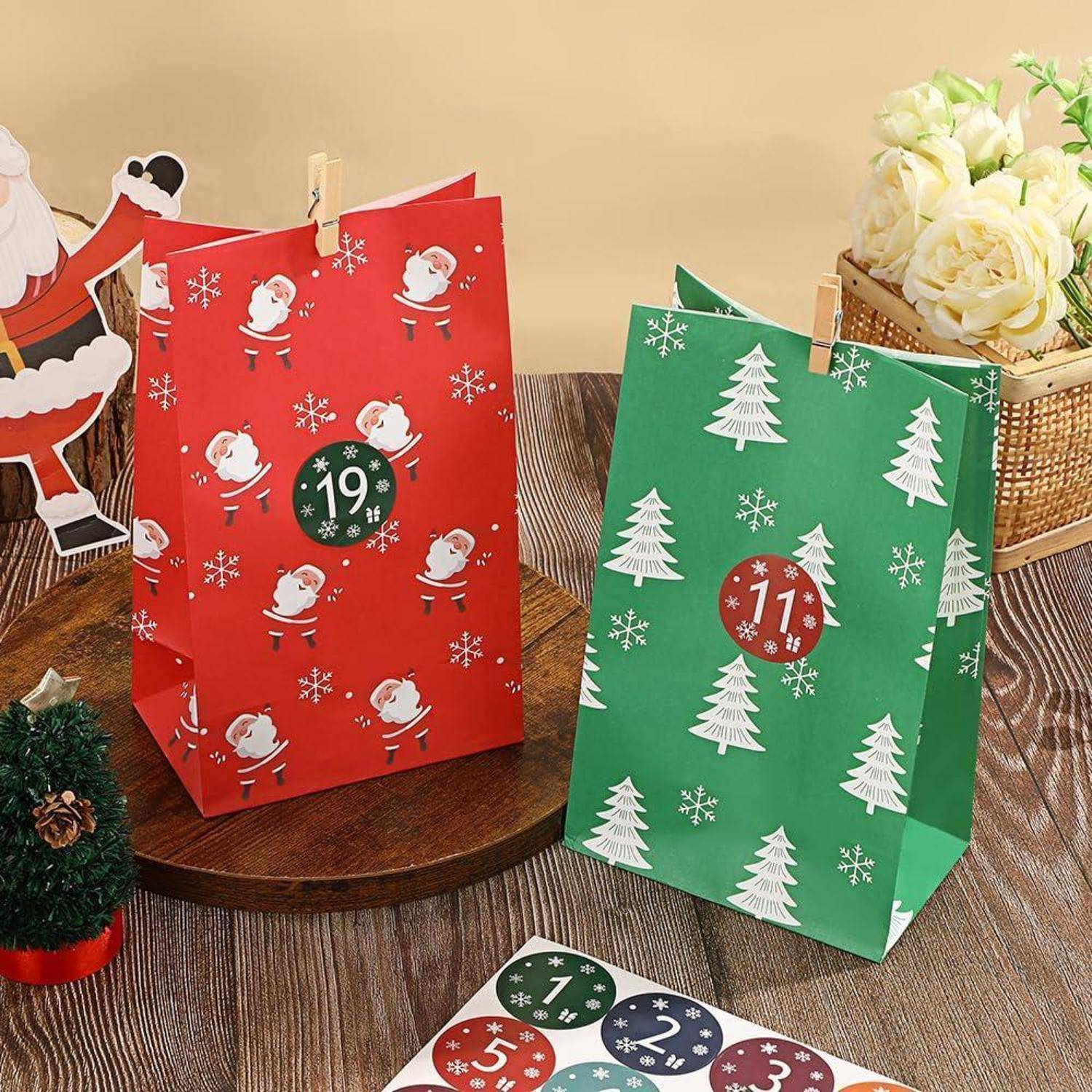 Festliche Weihnachtsgeschenktüten auf einem Tisch: rote Tasche mit Weihnachtsmannmuster mit der Nummer 19, grüne Tasche mit Baummuster mit der Nummer 11, und ein nummeriertes Kalenderblatt darunter.