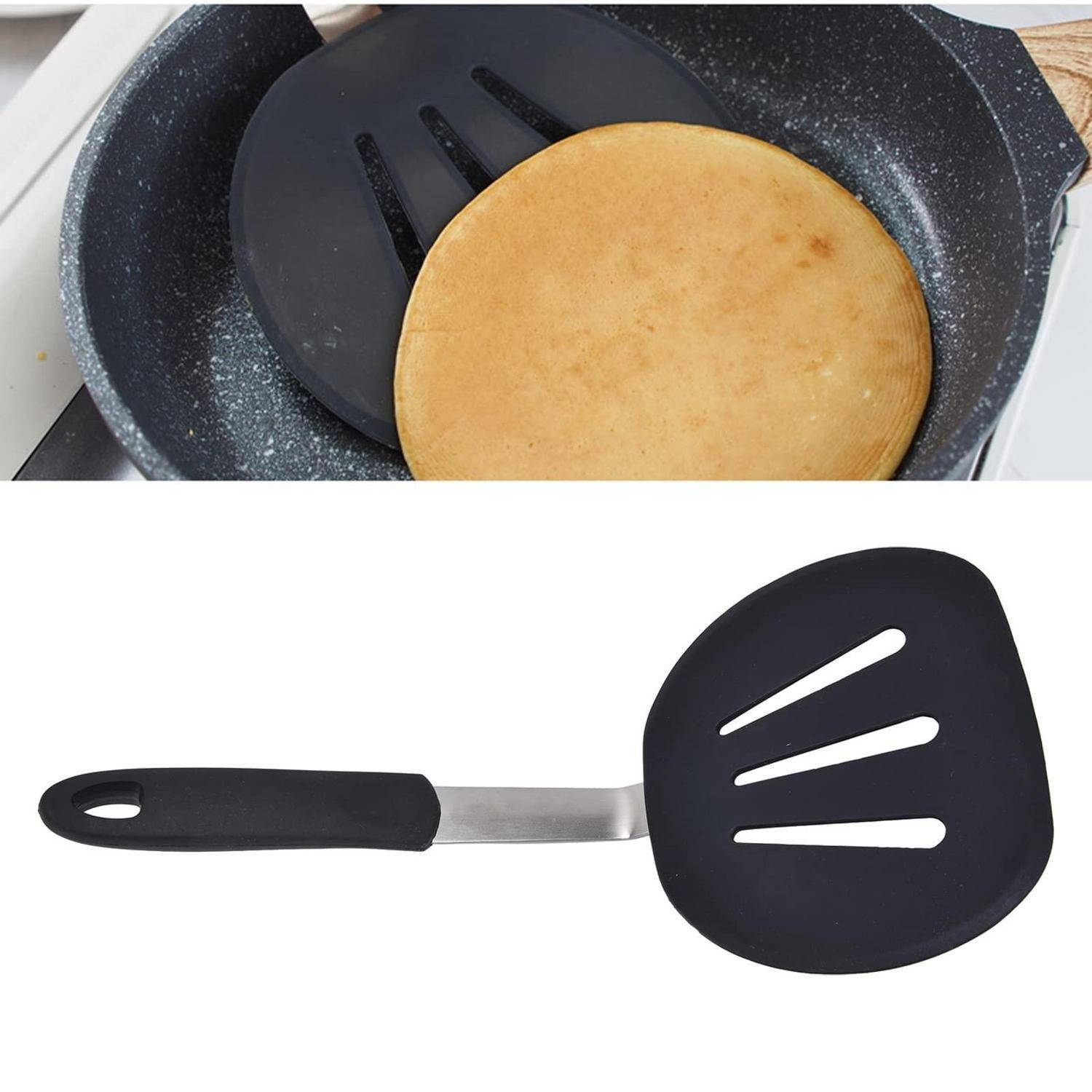 Schwarzer Pfannenwender mit Schlitzen, der einen Pfannkuchen in einer Pfanne hochhebt, mit dem Spatel darunter auf weißem Hintergrund angezeigt.