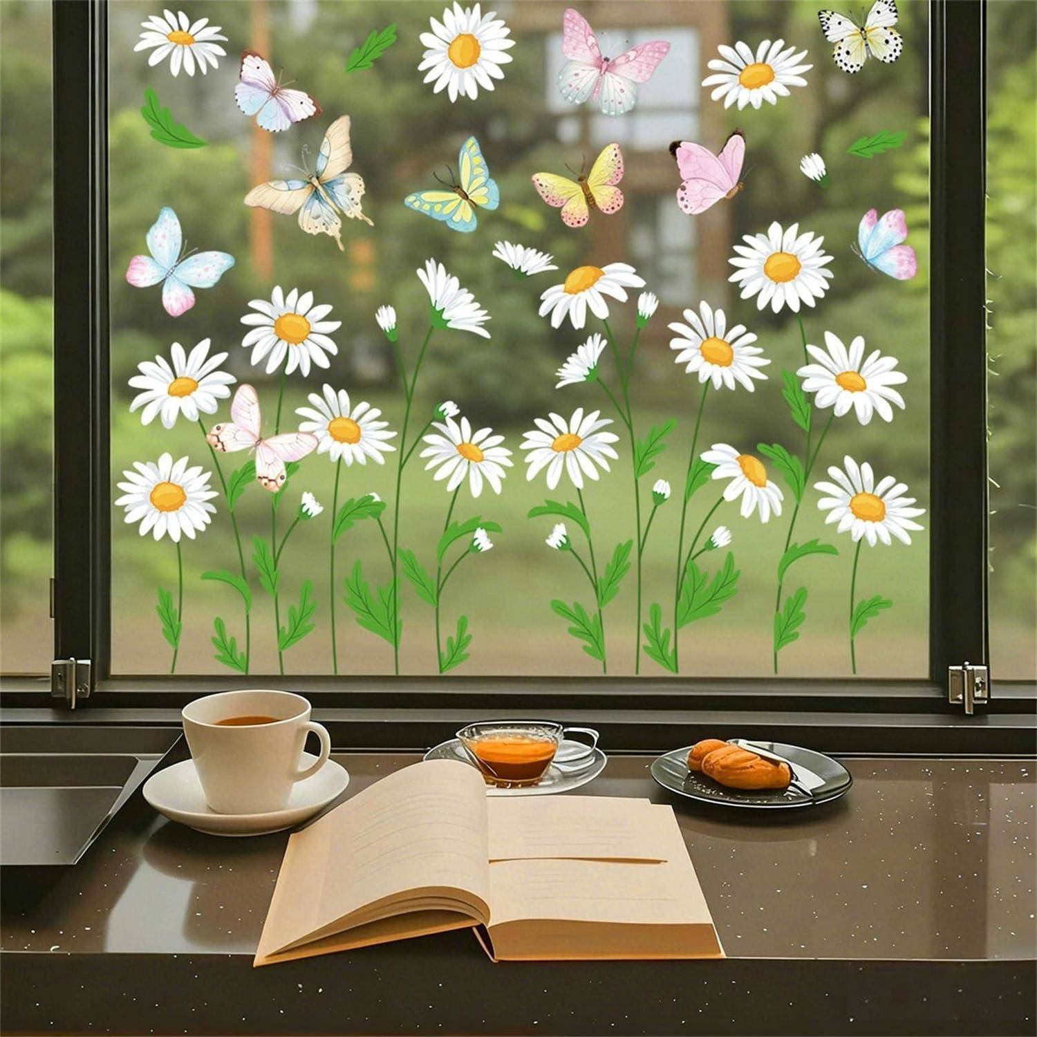 Ein aufgeschlagenes Buch neben einer Kaffeetasse und einem Gebäck auf einem Tisch neben einem Fenster, das mit Gänseblümchen- und Schmetterlings-Aufklebern verziert ist.