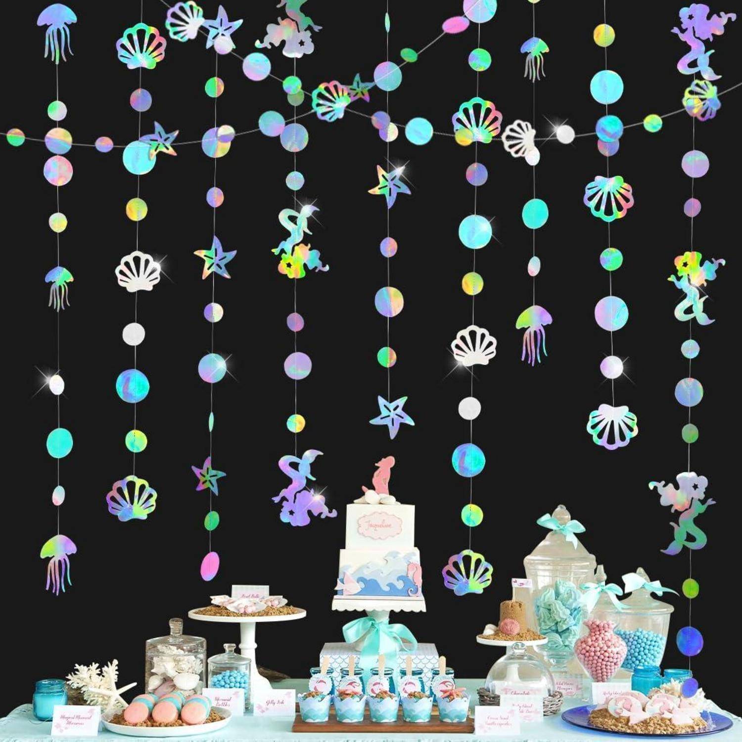 Unterwasser-themed Dessert-Tisch mit Pastellkuchen, Cupcakes, Keksen und Bonbongläsern unter hängenden irisierenden Meereskreaturen und Blasendekorationen vor schwarzem Hintergrund.