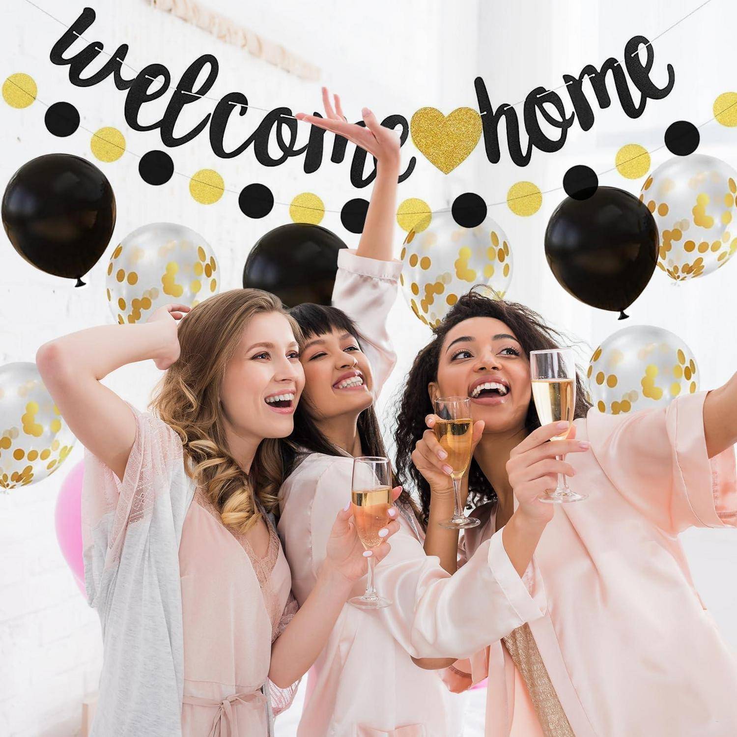 Drei Frauen in rosa Gewändern machen ein Selfie und stoßen mit Champagner auf einer "Willkommen zu Hause""-Feier mit Luftballons und Konfetti-Dekorationen an.