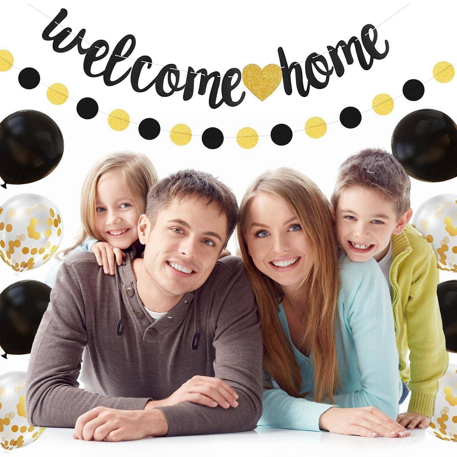 Lächelnde vierköpfige Familie posiert unter einem Banner mit der Aufschrift "Willkommen zu Hause"" mit schwarzen, goldenen und gepunkteten Luftballons.