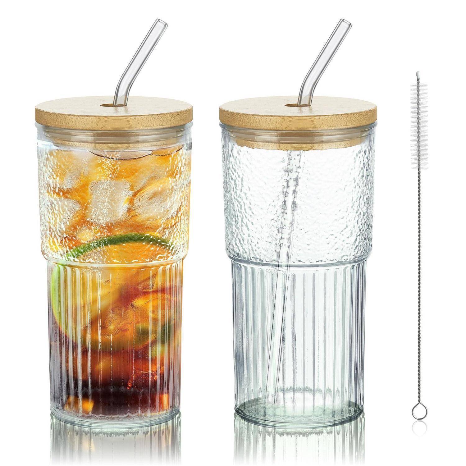Zwei gerippte Glastumbler mit Bambusdeckeln und wiederverwendbaren Strohhalmen, abgebildet mit einer Edelstahl-Strohhalm-Reinigungsbürste; ein Glas enthält ein Getränk mit Zitrusfrüchten und Eis.