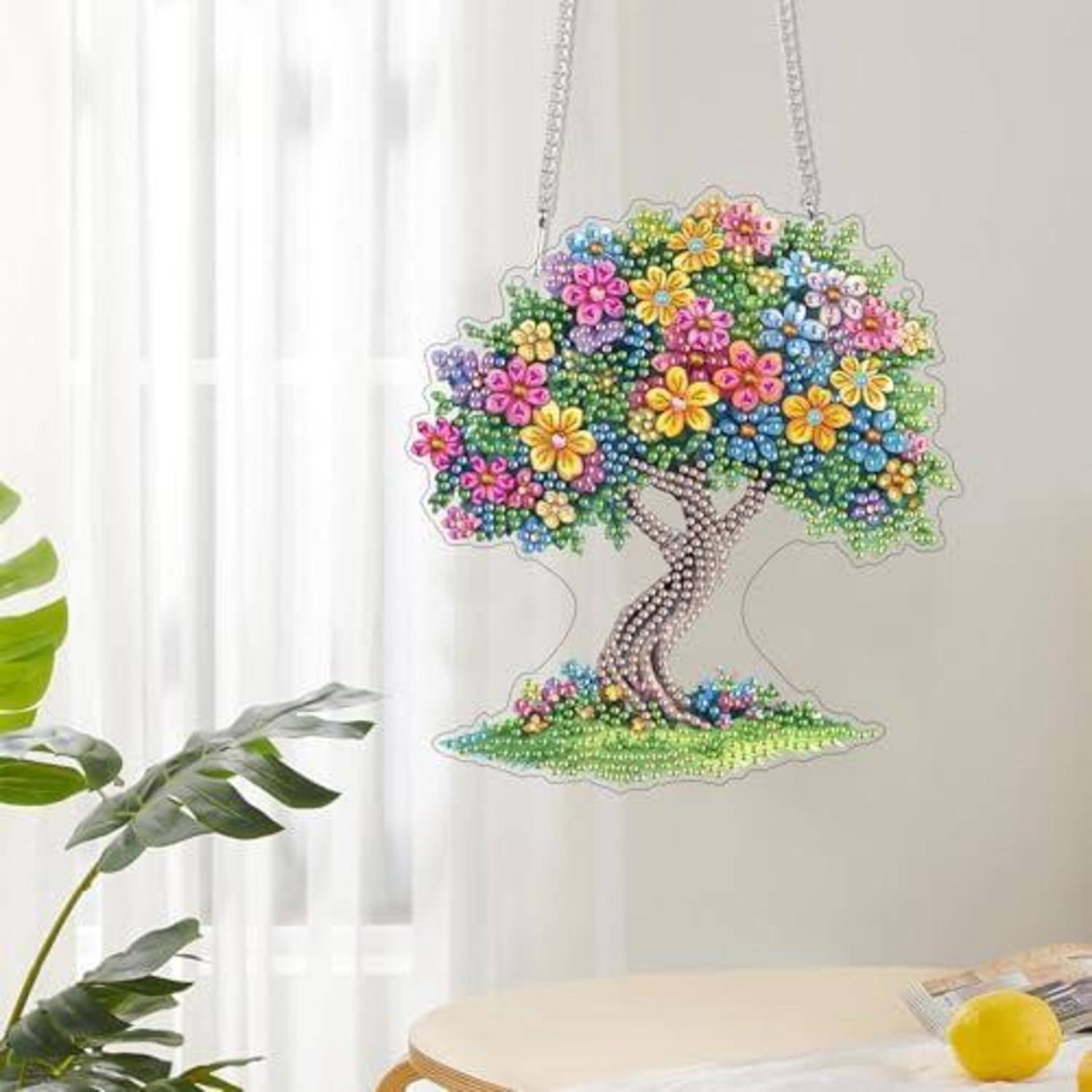 Behängter baumförmiger Wandschmuck aus Perlen mit farbenfrohen Blumen, aufgehängt in einem hellen Raum neben einem Fenster und einer Pflanze.
