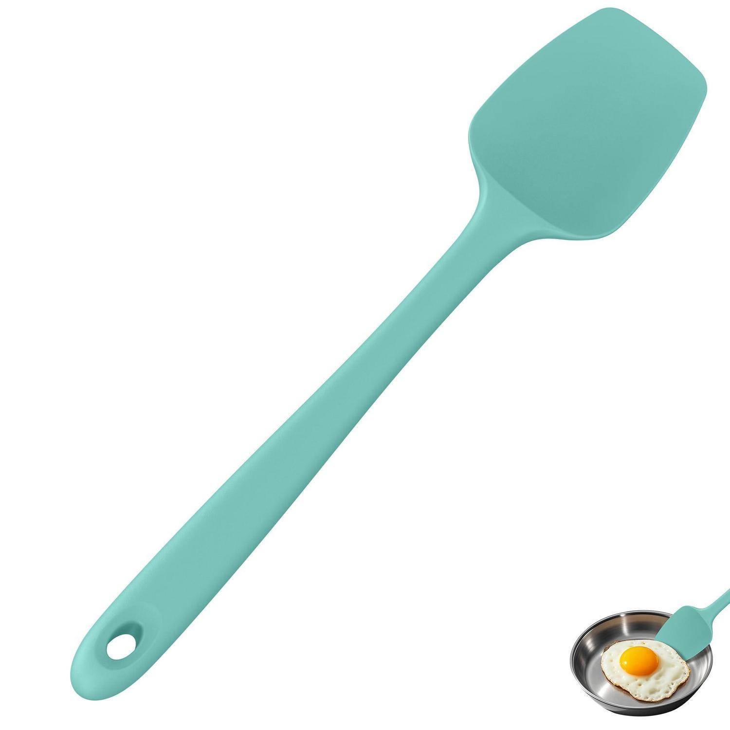 Minzgrüner Silikon-Spatel mit Aufhängeloch, abgebildet mit einer kleinen Pfanne, die ein Spiegelei enthält, um die Verwendung beim Kochen zu veranschaulichen.