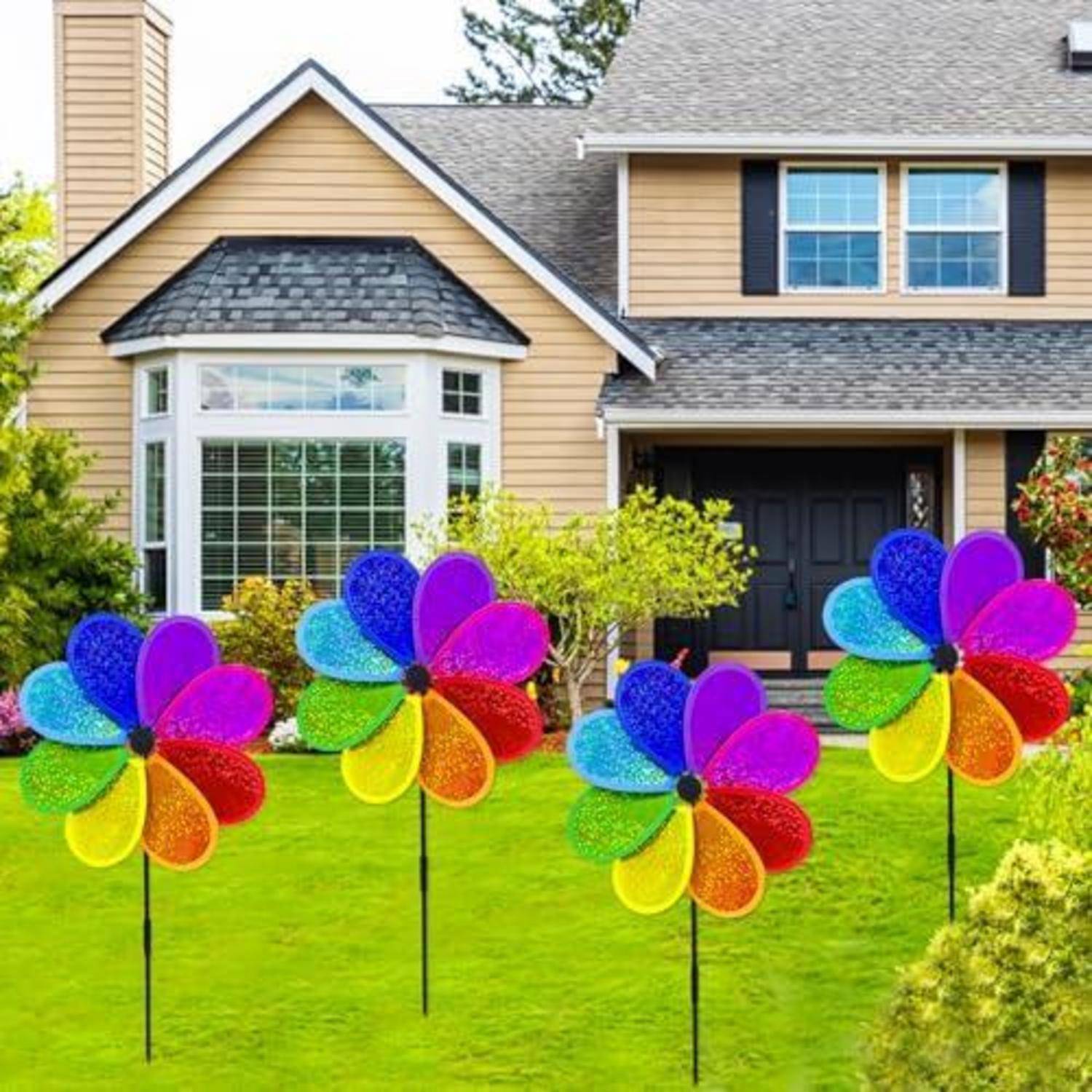 Vier bunte Windmühlen-Gartendekoration auf Stäben in einem Vorgarten mit einem Einfamilienhaus im Hintergrund.