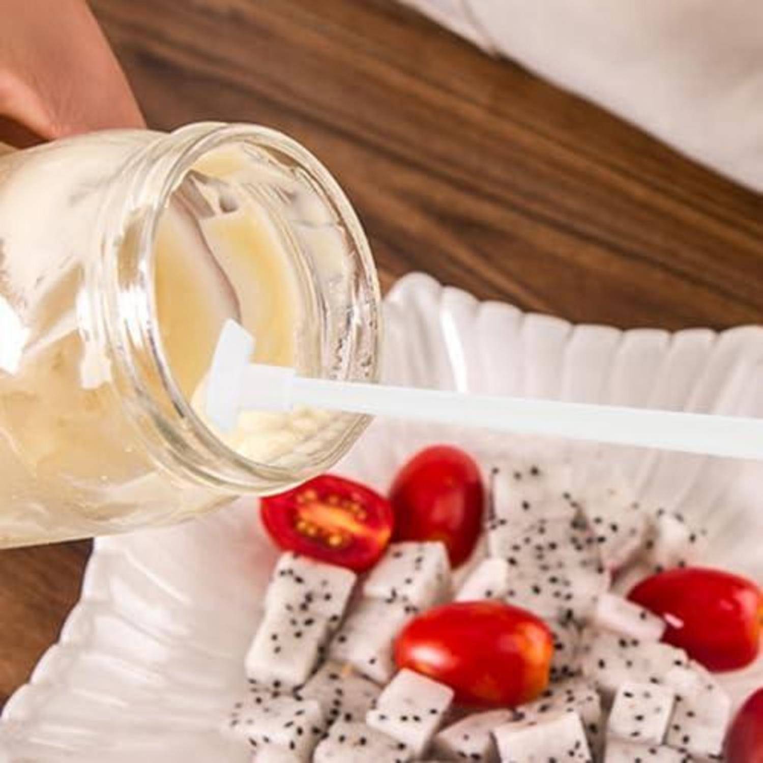 Cremiges Salatdressing wird aus einem Glas in eine Schüssel mit Salat, Kirschtomaten und sesamähnlichen Samen gegossen.