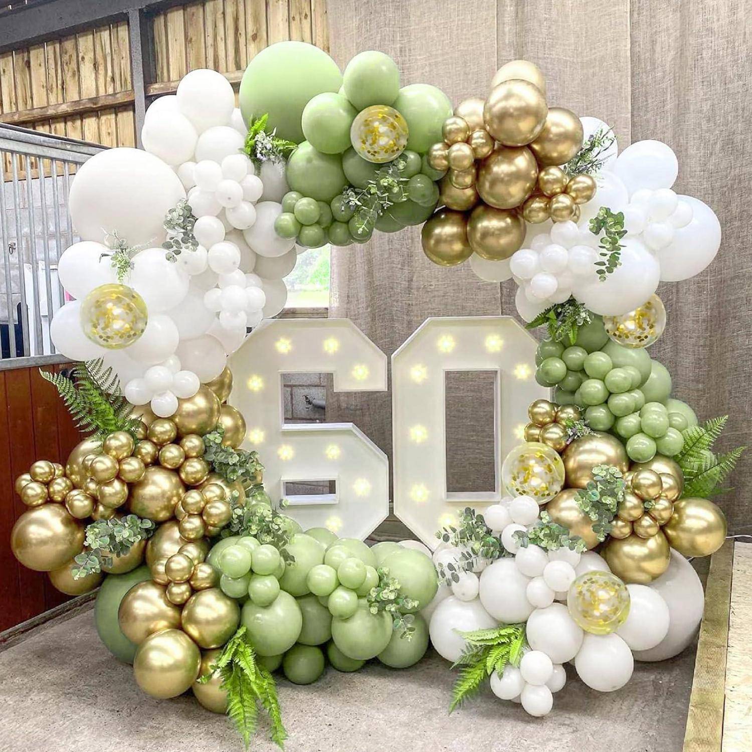 Beleuchtete „60" umgeben von einer großen Ballongirlande in Grün, Weiß und Gold, die eine Feier zum 60. Geburtstag suggeriert.