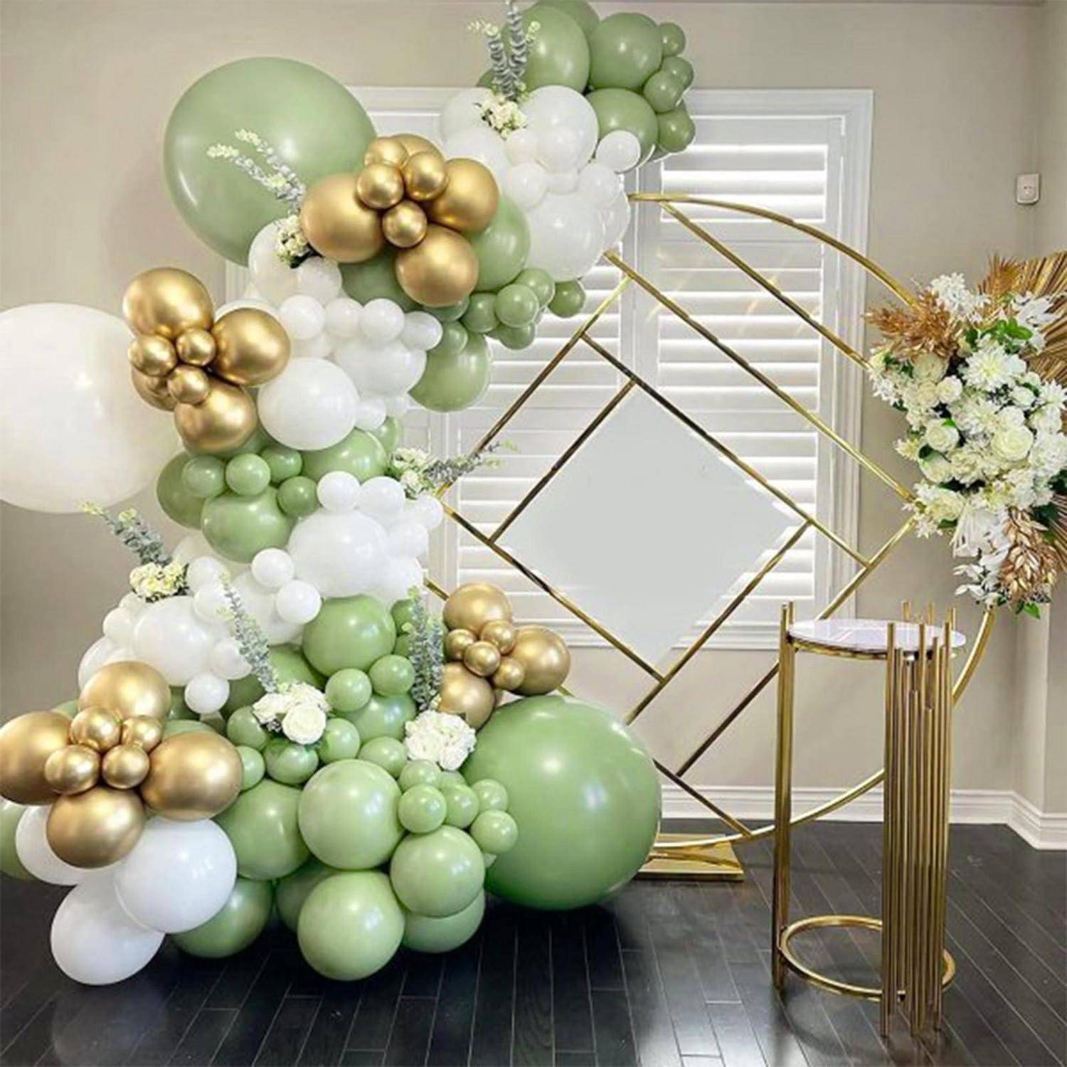 Pastellgrüne, weiße und goldene Ballonblumendeko mit geometrischem goldenem Hintergrund und kleinem Goldsockel, aufgebaut für eine Veranstaltung oder Feier.