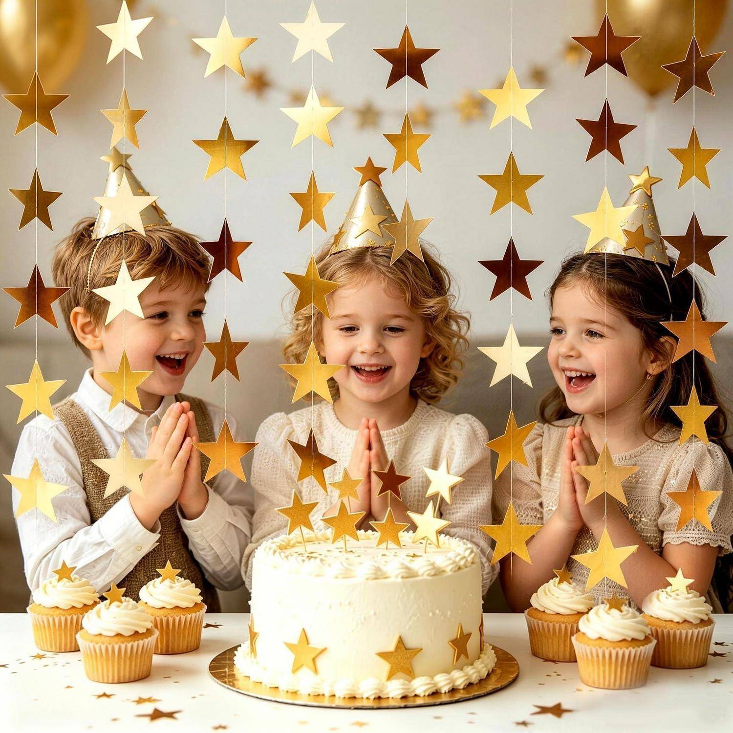 Drei Kinder mit Partyhüten lächeln und klatschen um einen Geburtstagskuchen und Cupcakes herum, die hinter goldenen Sterndekorationen angeordnet sind.