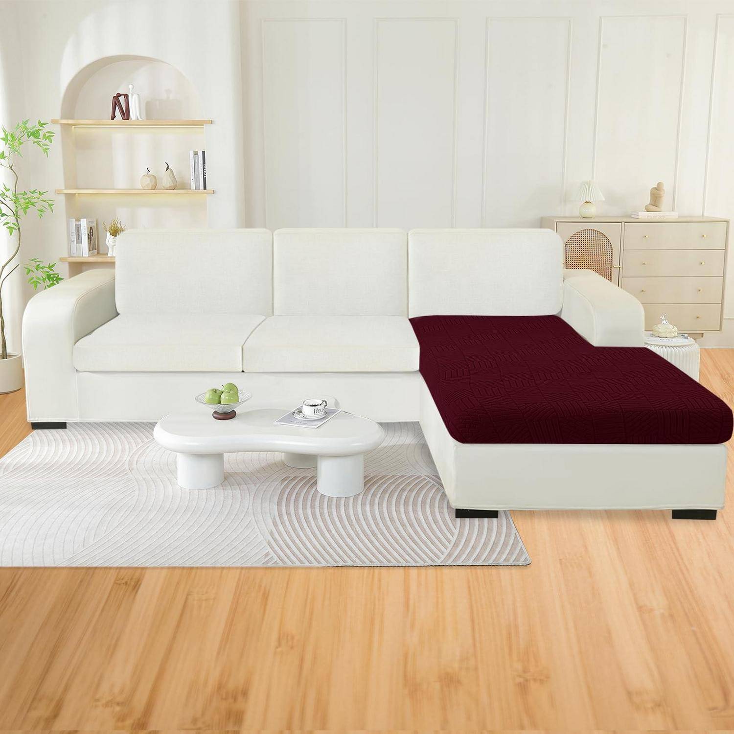 Weißes Ecksofa mit einer burgunderroten Chaiselongue in einem hellen Wohnzimmer, neben einem kleinen weißen Couchtisch und hellholzmöbeln.