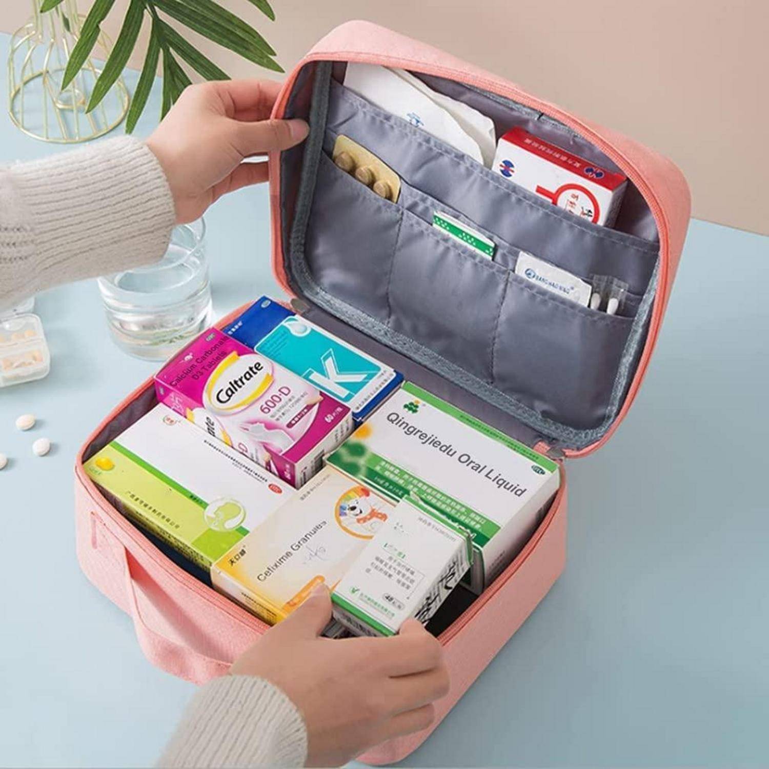 Hände öffnen einen rosa Erste-Hilfe-Organizer, der mit verschiedenen Medikamenten und Boxen mit oralen Flüssigkeiten auf einem Tisch gefüllt ist.