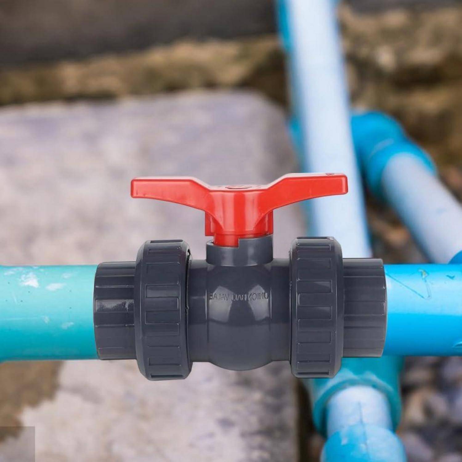 Nahaufnahme eines Ventils mit rotem Griff an einem blauen PVC-Rohr, das eine Wasserkontroll-Absperrung in einer Außen-Sanitäranlage zeigt.