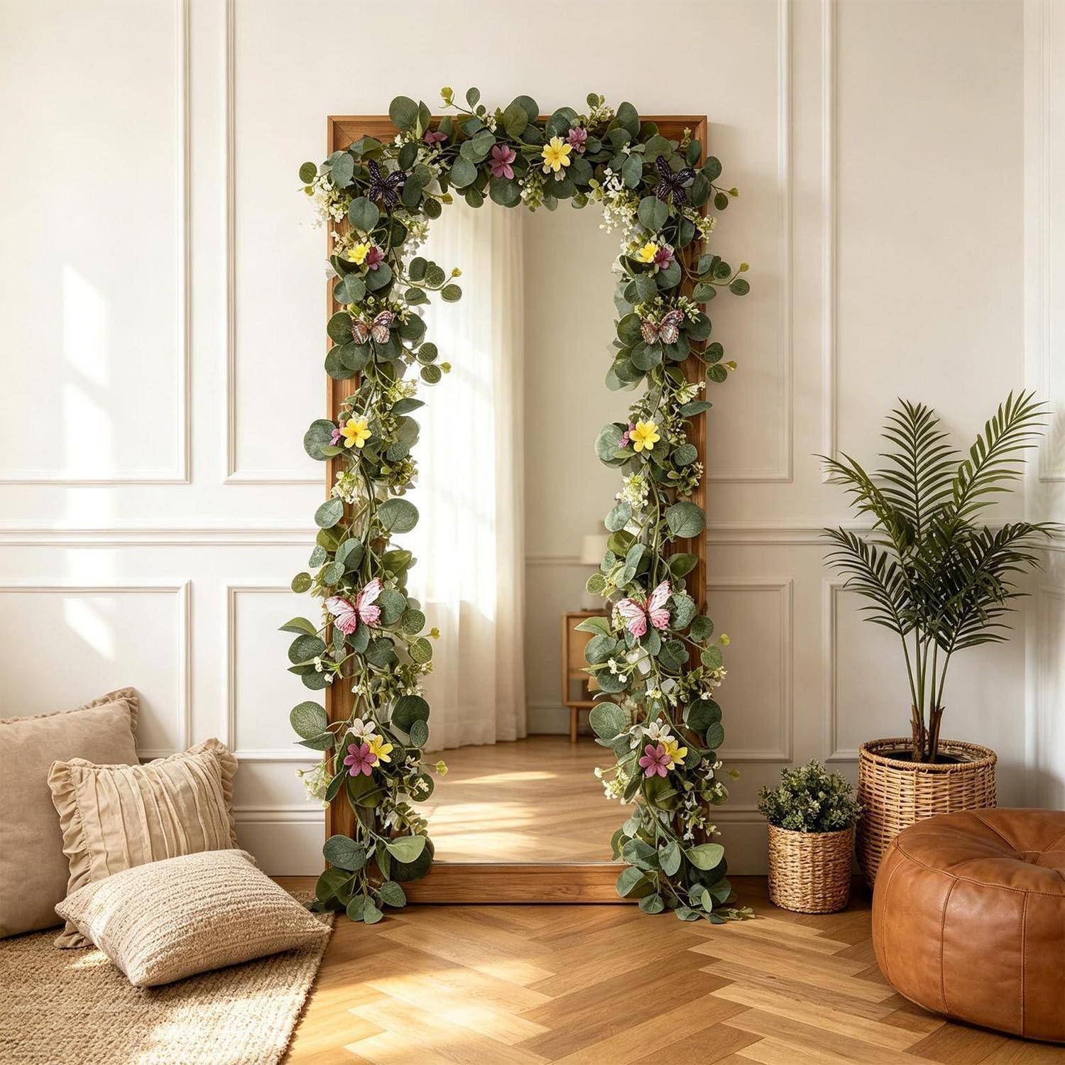 Innenspiegel, umrahmt von einer üppigen Blüten- und Blattgirlande in einem hellen, eleganten Wohnzimmer mit Kissen, Pflanzen und einem Lederpouf.