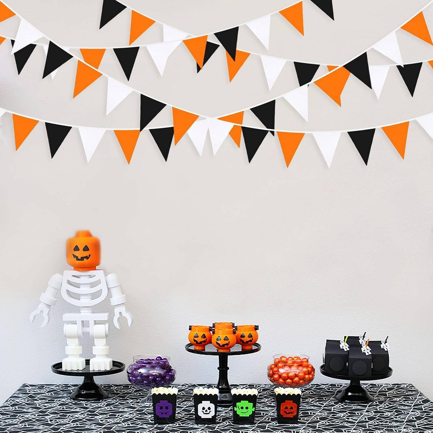 Halloweens-Nachtischtisch mit Kürbiskopf-Skelett-Figur, Jack-o'-Lantern-Süßigkeiten und orange-schwarz-weißer Wimpelkette auf einer Spinnennetz-Tischdecke.