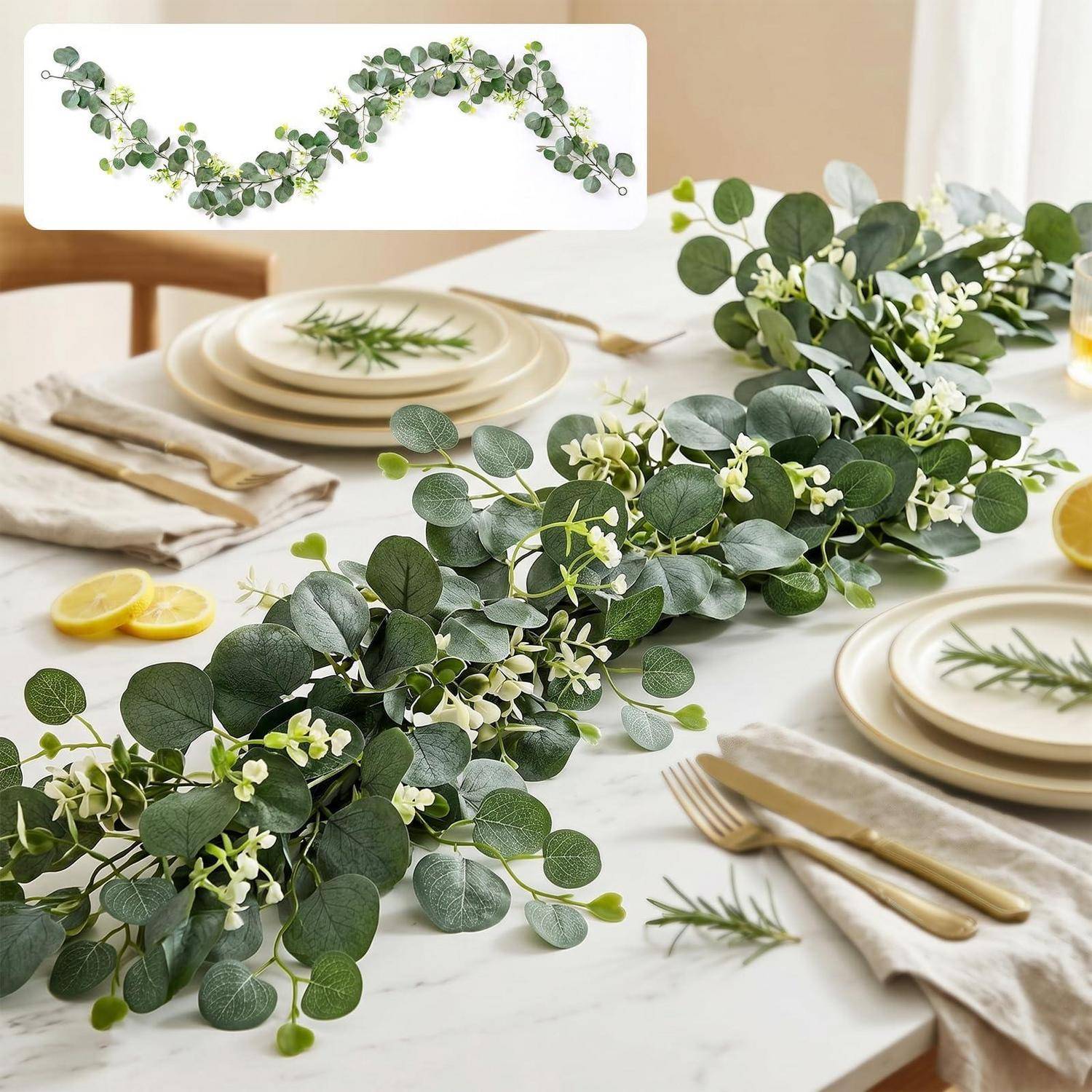Eukalyptus- und Weißblüten-Girlanden-Mittelstück, das einen eingedeckten Esstisch mit Tellern, Servietten, goldenem Besteck und Zitronenscheiben dekoriert.