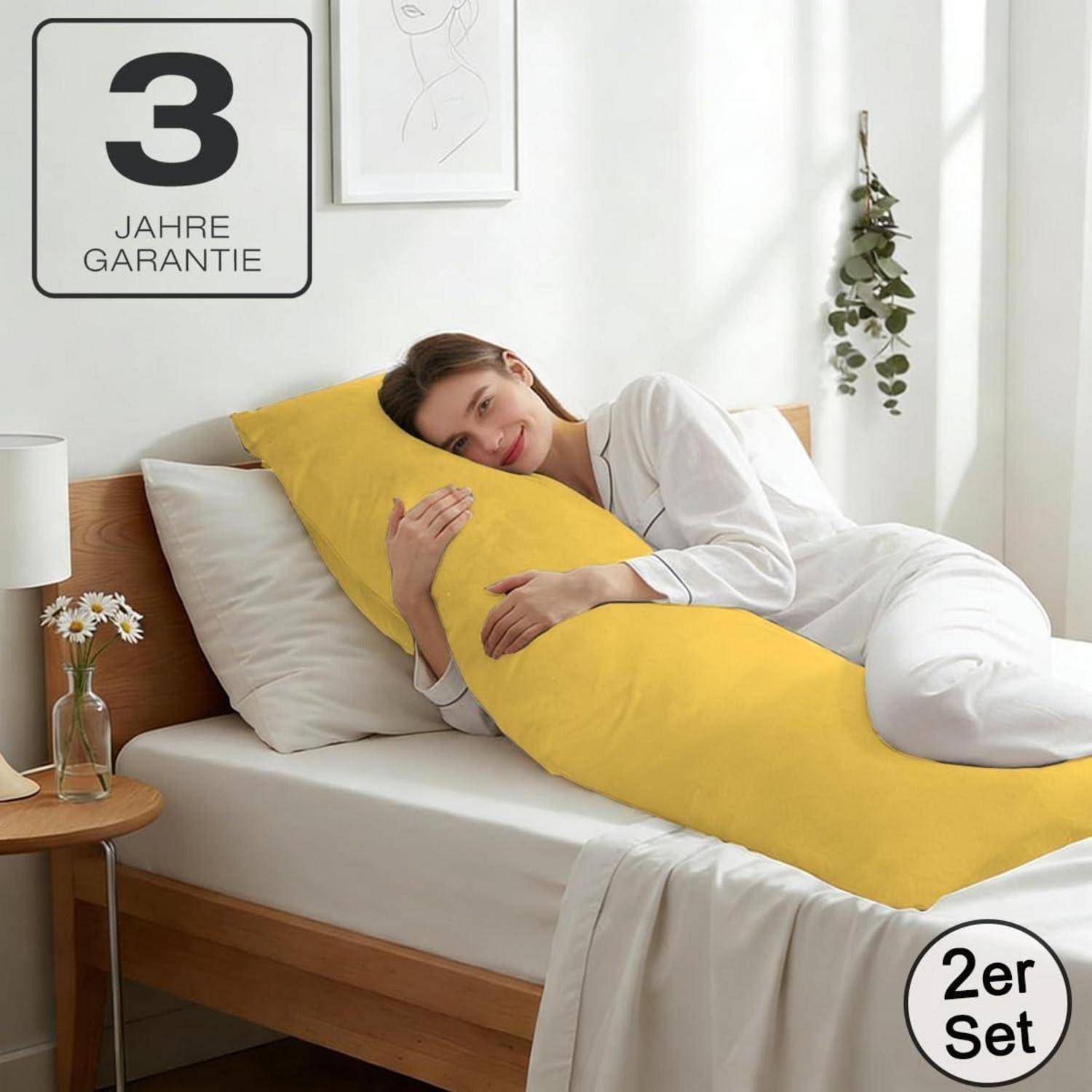 Frau im weißen Pyjama umarmt ein langes gelbes Körperkissen auf einem Bett; Produktabzeichen zeigen „3 JAHRE GARANTIE