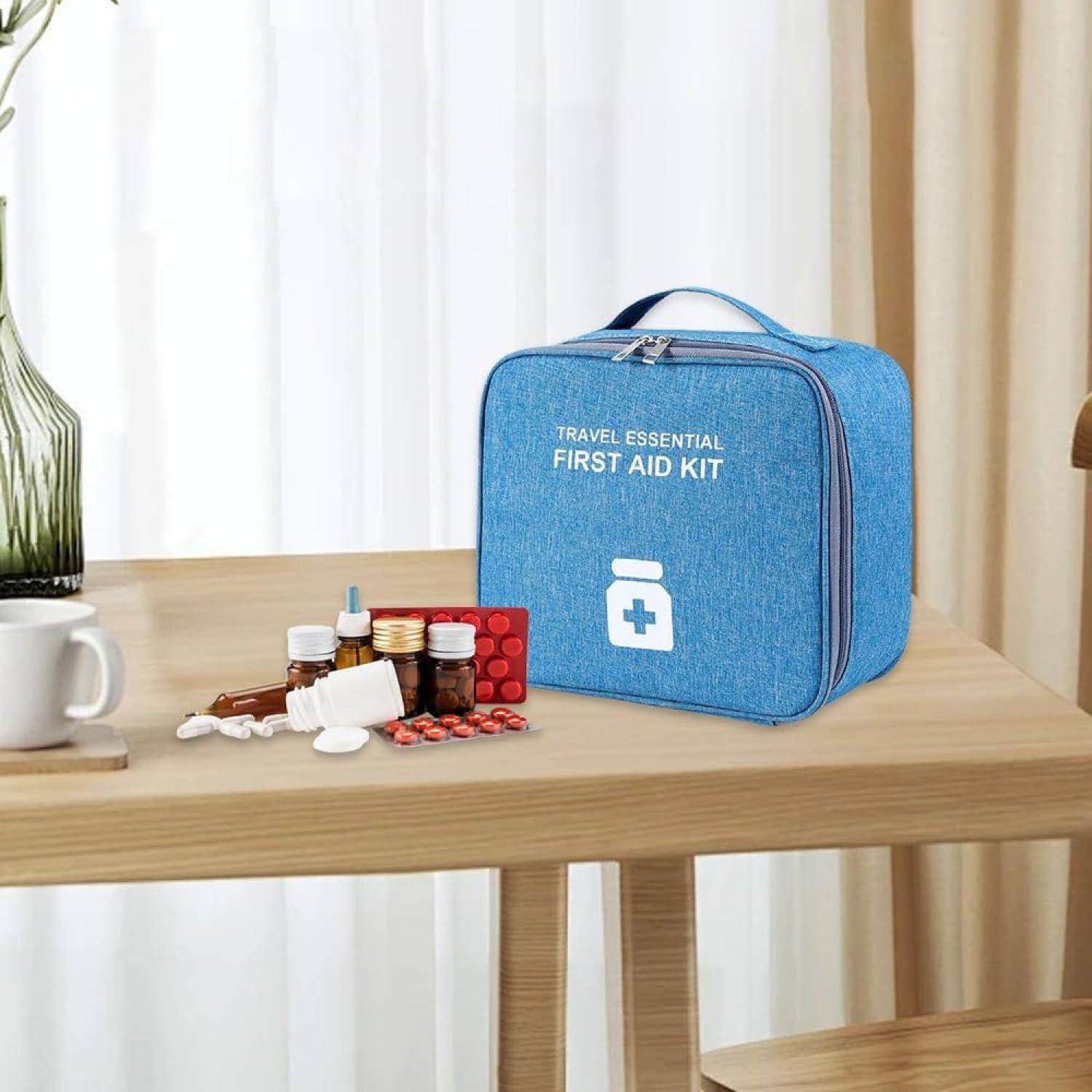 Blaue Reise-Erste-Hilfe-Tasche auf einem Tisch mit verschiedenen Medikamentenflaschen, Tabletten und Kapseln daneben.