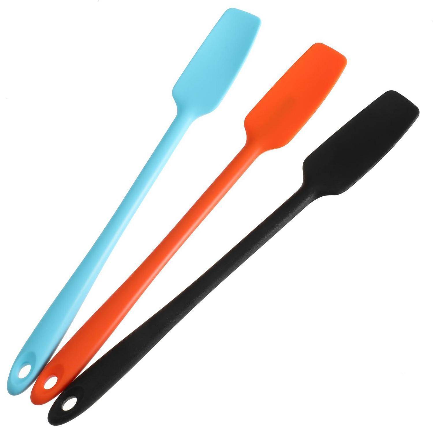 Drei Silikonspatel in Hellblau, Orange und Schwarz, diagonal auf weißem Hintergrund angeordnet.