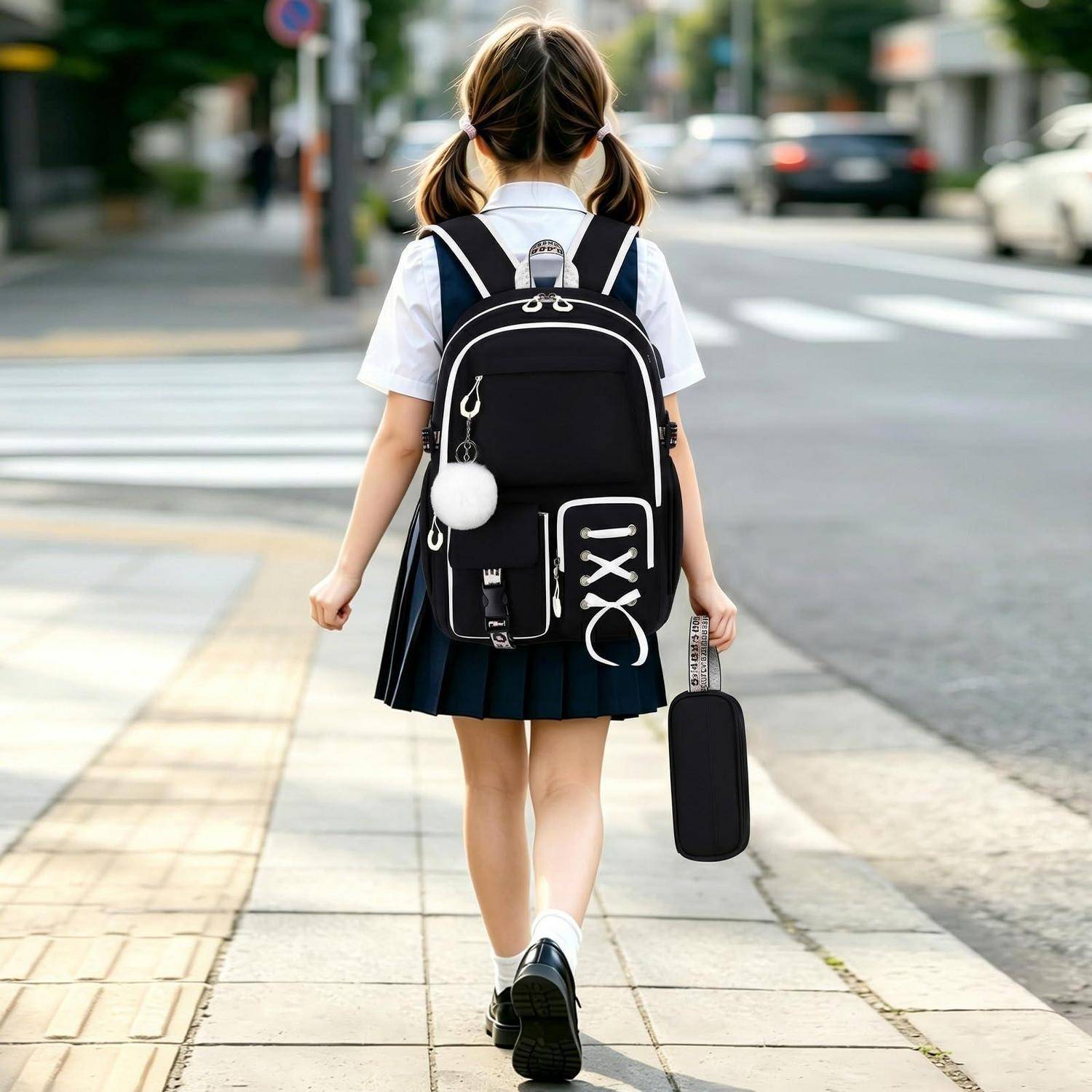 Junges Schulmädchen in Uniform mit einem Rucksack, das allein auf einem Gehweg der Stadt spaziert, einen kleinen Koffer tragend, von hinten an einem Zebrastreifen gesehen.