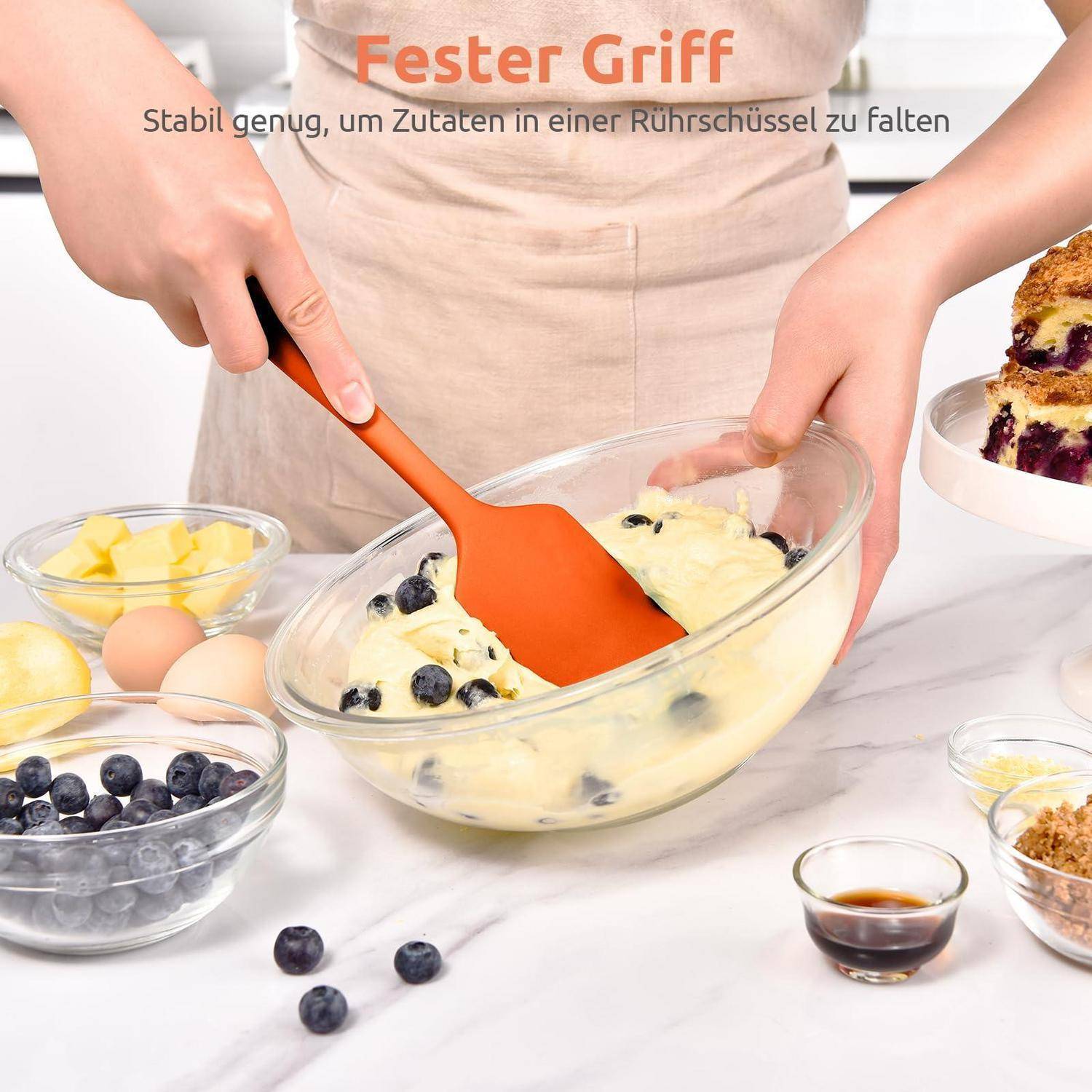 Person mit einem orangefarbenen Spatel mit stabilem Griff zum Unterheben von Blaubeeren in den Teig in einer Glassrührschüssel; Text sagt 