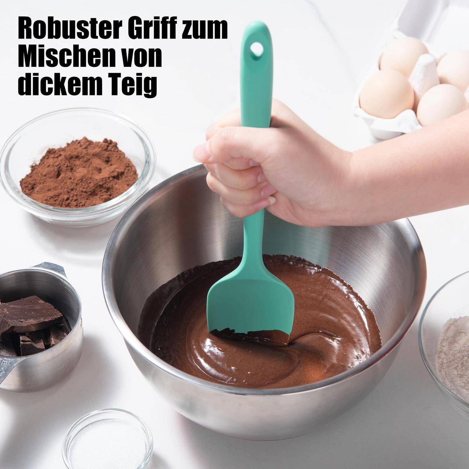 Handgerührte dicke Schokoladenmasse in einer Metallmischschüssel mit einem grünen Spatel, umgeben von Kakaopulver, Schokoladenstücken und Eiern; Text lautet „Robuster Griff zum Mischen von dickem Teig