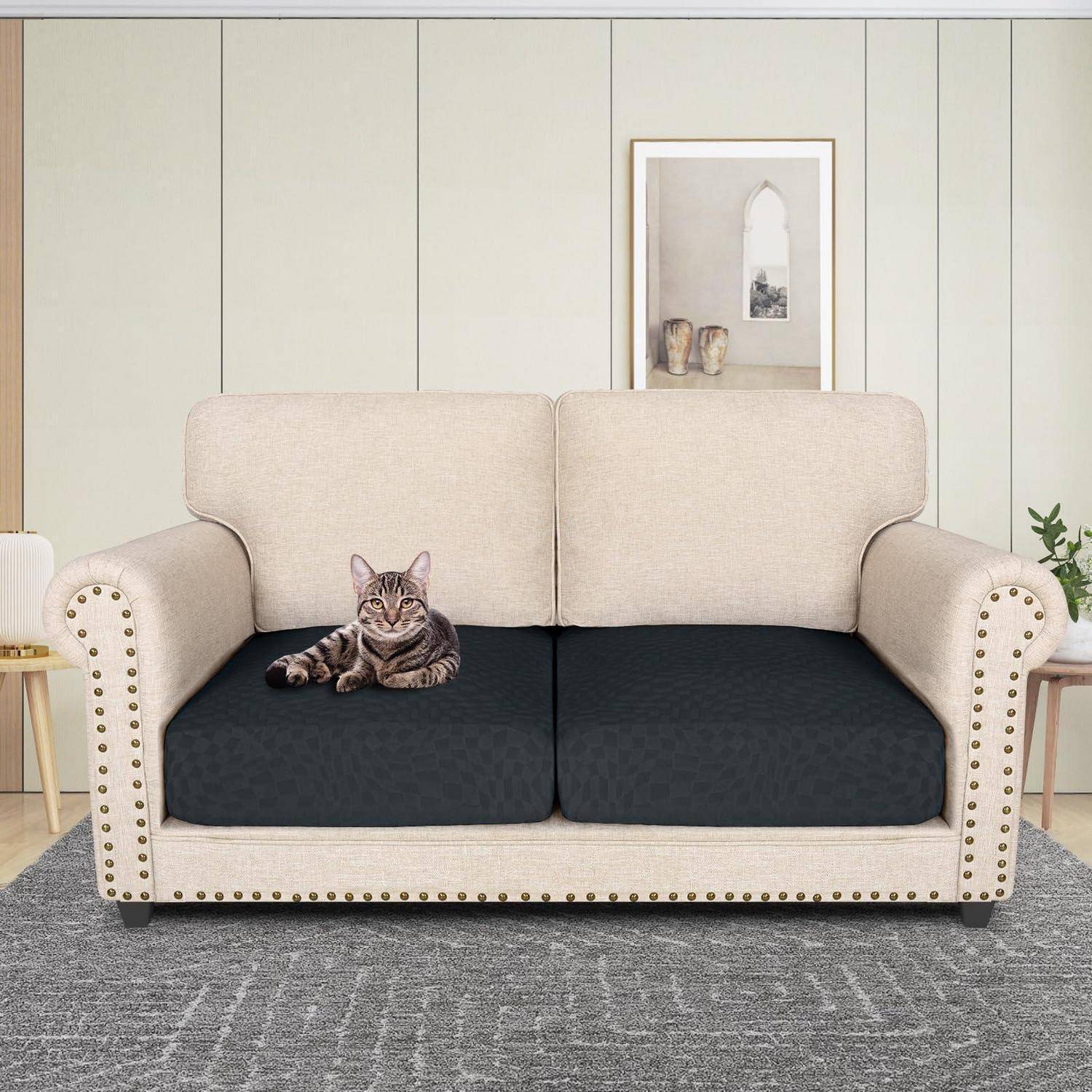 Eine getigerte Katze liegt auf einem beige Zweisitzer-Sofa mit dunklen Kissen in einem hellen Wohnzimmer.