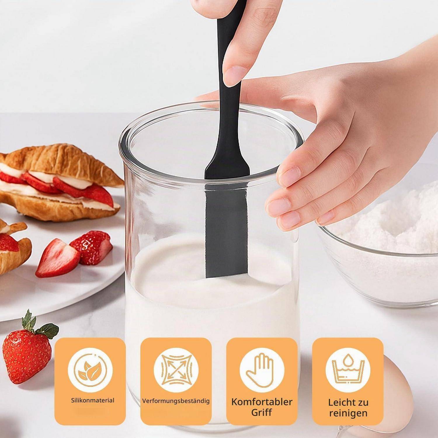 Hände, die eine weiße Flüssigkeit in einem klaren Glas mit einem schwarzen Spatel vermischen; Erdbeeren und Gebäck in der Nähe, mit Funktionssymbolen für Silikonmaterial, Formbeständigkeit, komfortabler Griff und einfache Reinigung.