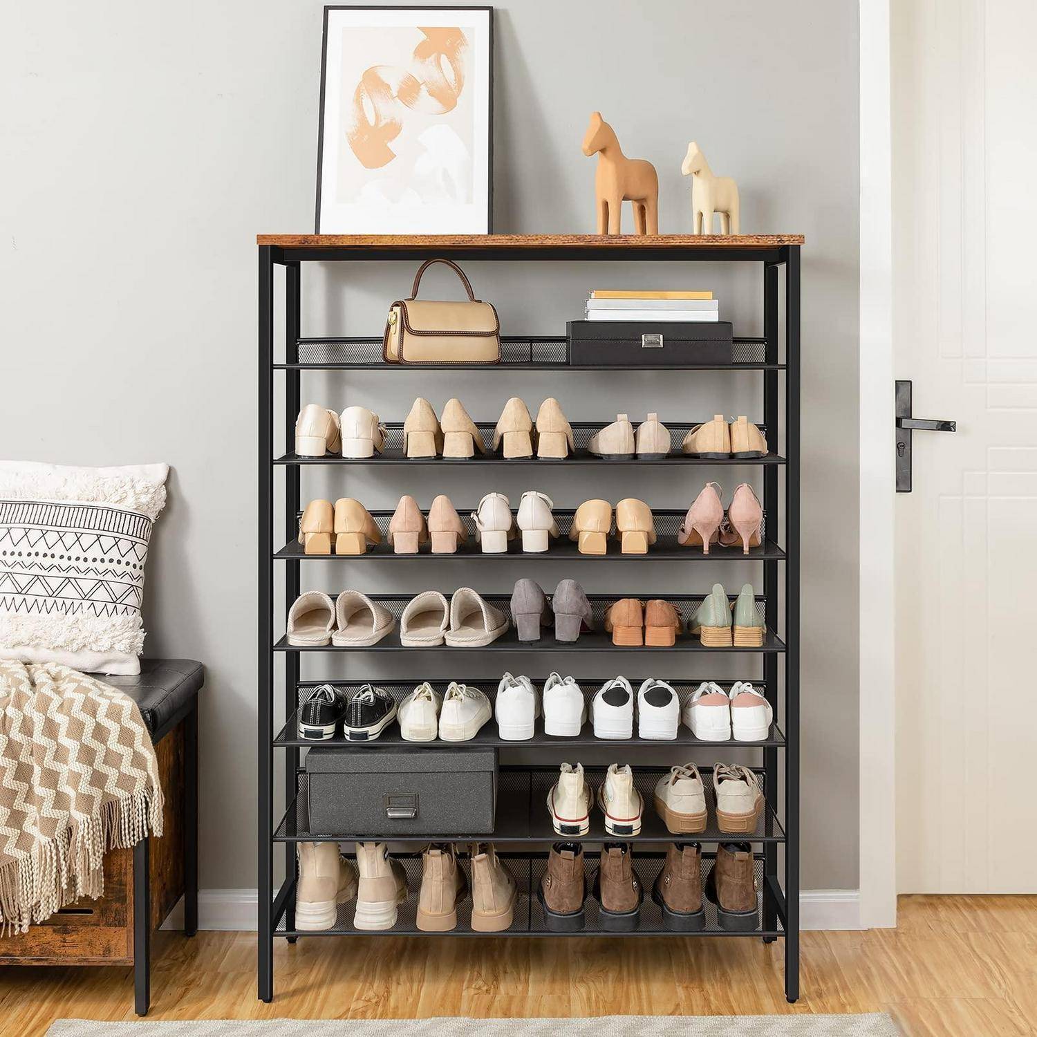 Schuhregal mit vielen ordentlich angeordneten Schuhpaaren in einem Schlafzimmer, plus einer Handtasche, Aufbewahrungsboxen und kleinen Dekorationselementen oben.