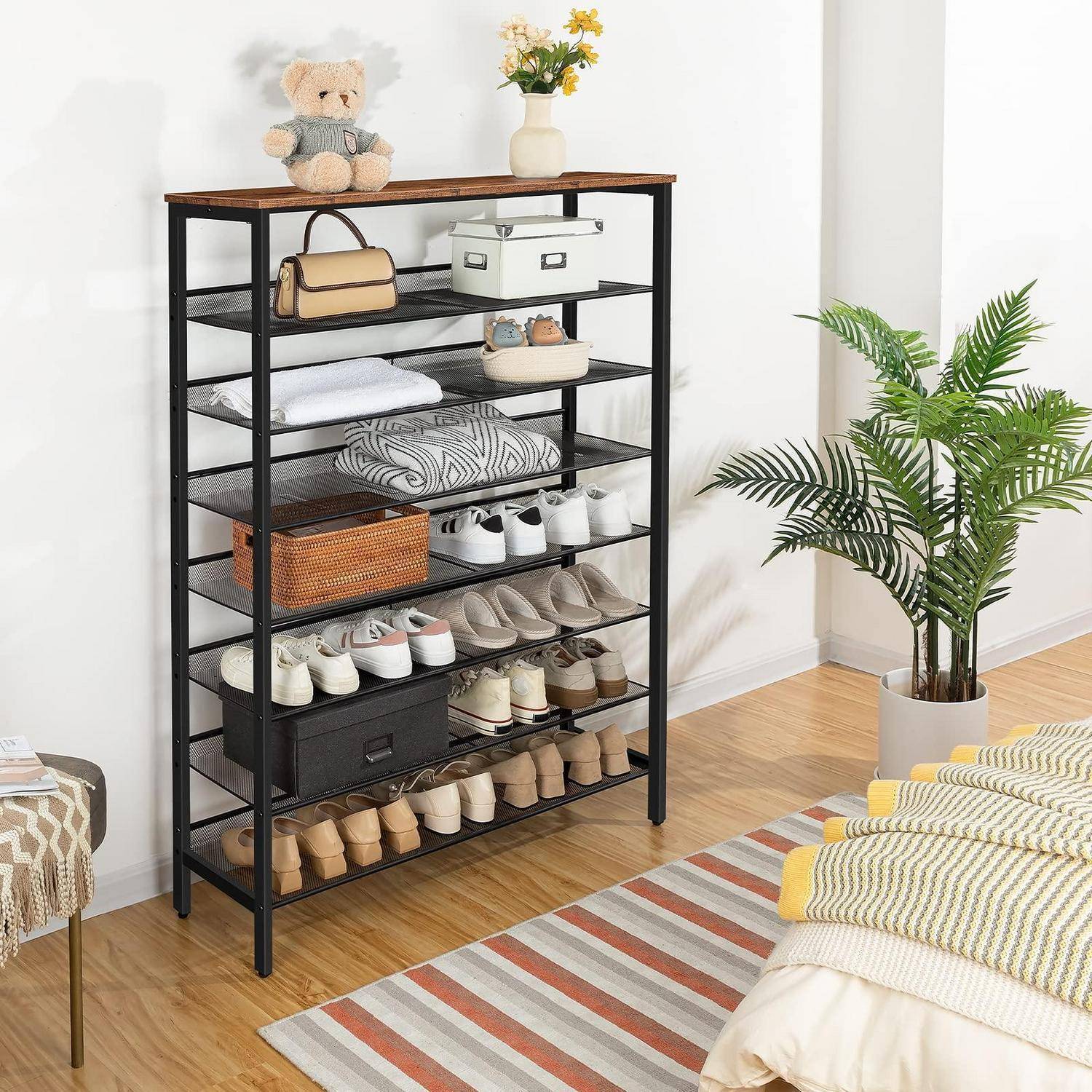 Hohe schwarze Regalserie, die als Schuh- und Aufbewahrungsorganizer verwendet wird und Schuhe, Taschen, gefaltete Handtücher und Körbe in einem hellen Raum mit einer Pflanze und einem Teppich enthält.