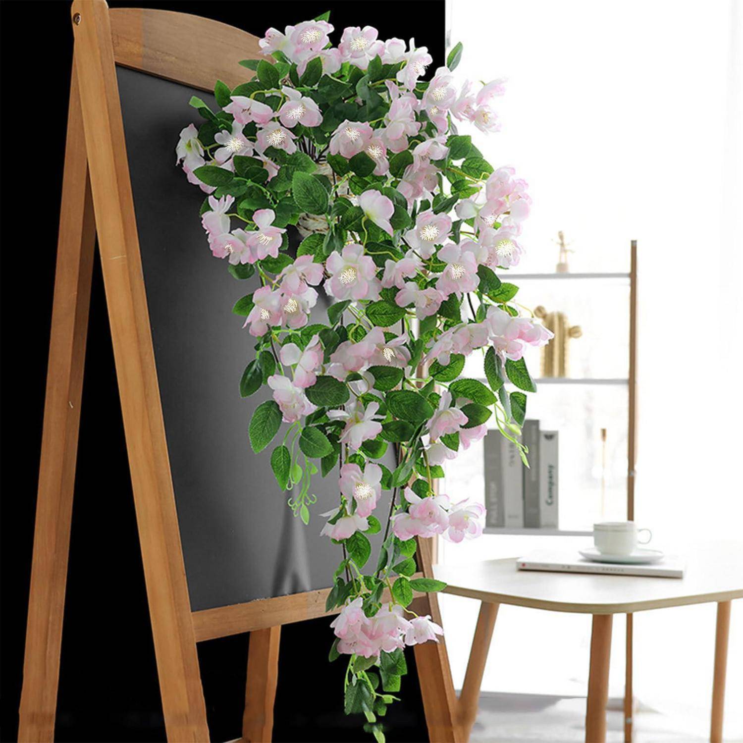 Künstliche hängend rosa-weiße Blüten drapieren sich über eine schwarze Tafel mit Holzrahmen neben einem kleinen Tisch in einem hellen Raum.