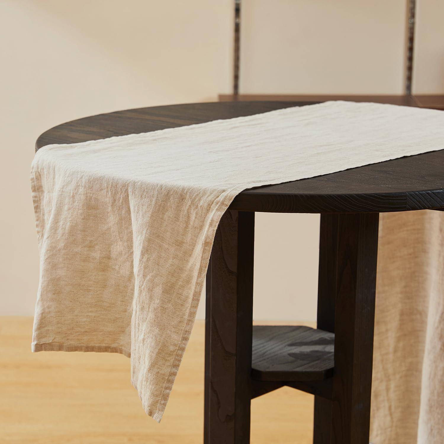 Dunkler runder Tisch mit einem weißen Leinenläufer, der über die Kante drapiert ist, in einem minimalistischen Raum.