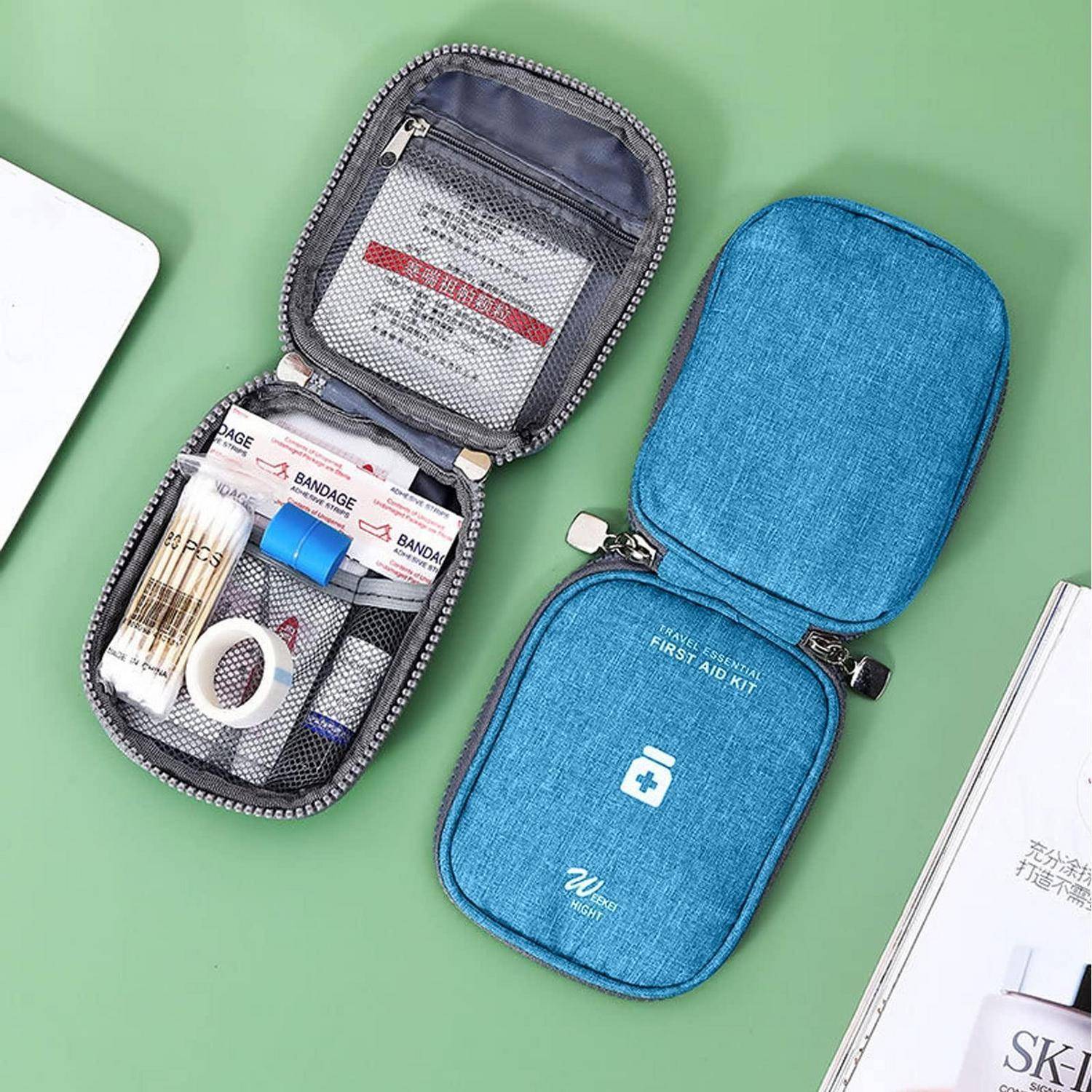 Zwei kleine Erste-Hilfe-Sets mit Reißverschluss auf einer grünen Oberfläche, eines offen mit Verbandsmaterial, Klebeband und Vorräten, das andere geschlossen in blauem Denim.