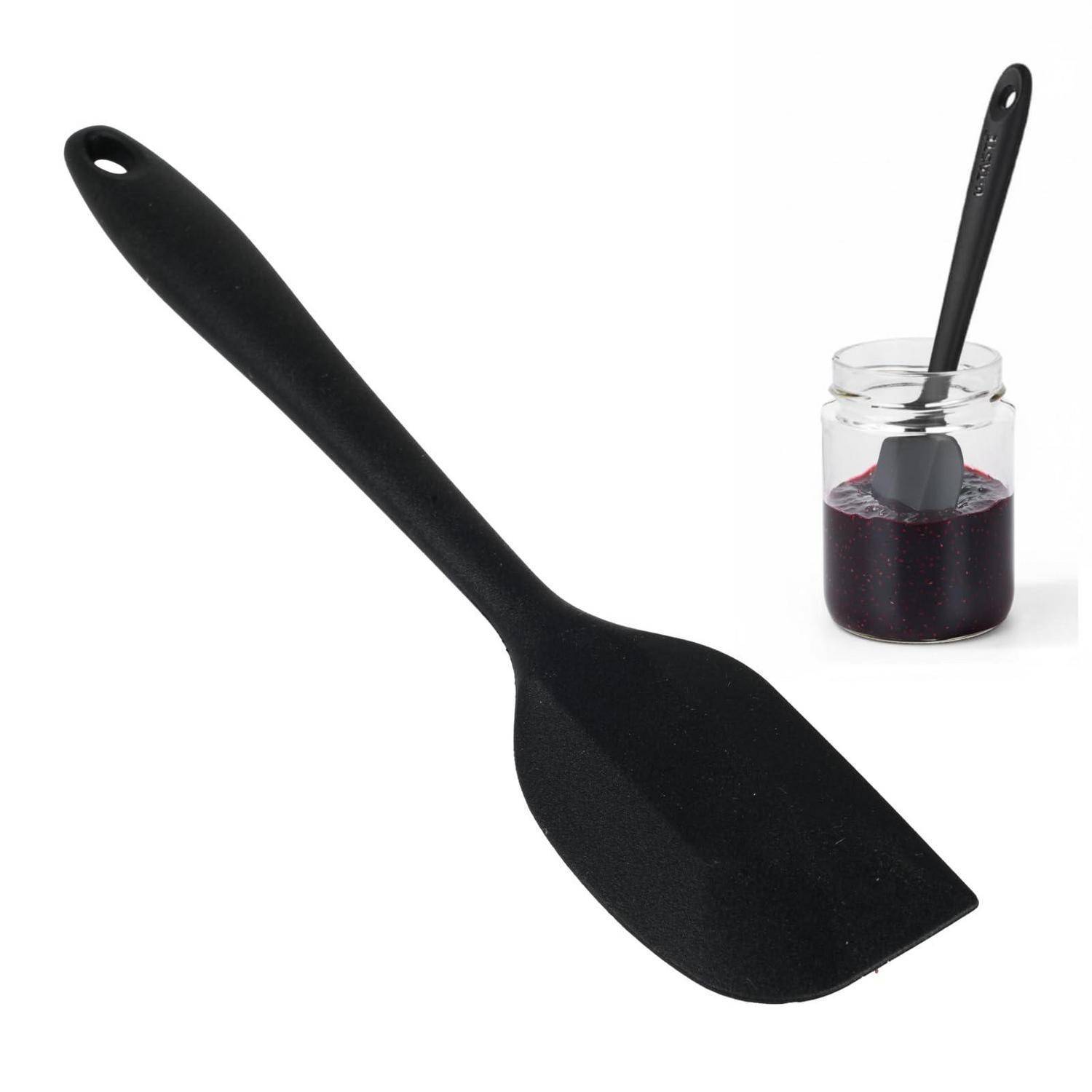 Schwarze Silikonspatula und Glas mit passender Spatula, getaucht in dunkle Marmelade oder Sauce auf weißem Hintergrund.