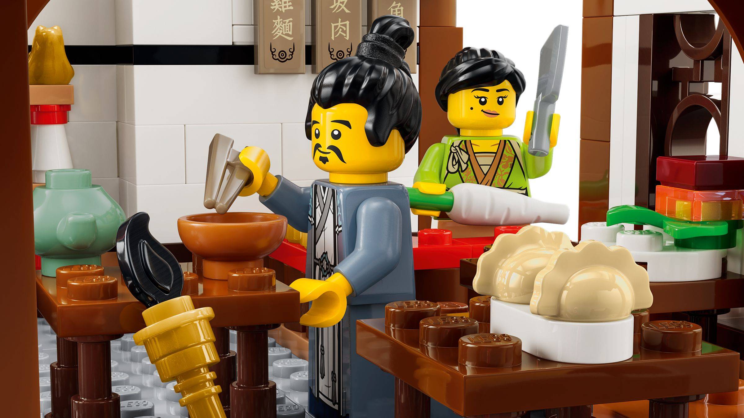 Legoähnlicher Essensstand mit zwei Figuren, die Lebensmittel zubereiten; eine Figur hackt Zutaten in einer Schüssel, während eine andere dahinter mit einem Hackebeil steht.