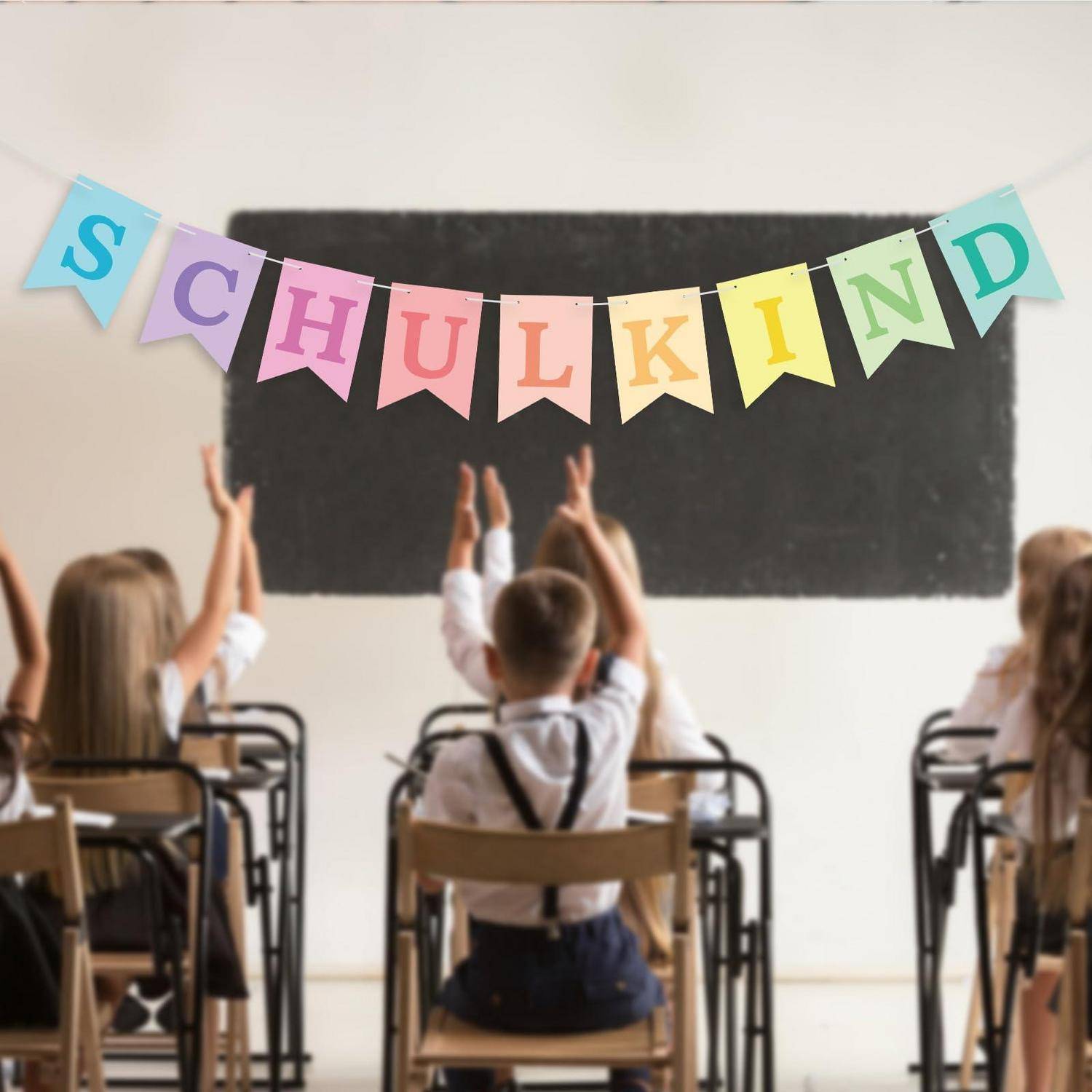 Kinder in einem Klassenzimmer strecken ihre Hände zur Tafel, wobei ein buntes Banner mit der Aufschrift „SCHULKIND" darüber hängt.