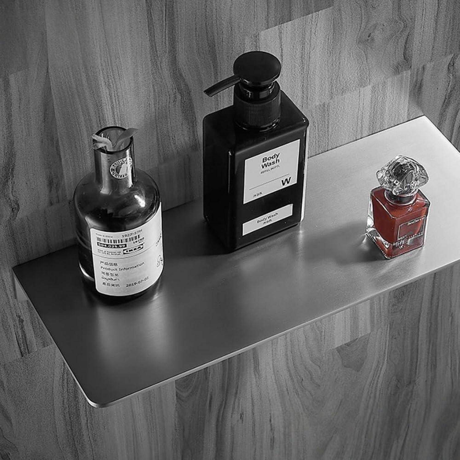Drei Toilettenflaschen auf einem an der Wand angebrachten Regal, darunter eine schwarze Pumpflasche für „Körperwaschmittel" und eine kleine rote Parfümflasche, vor Holzvertäfelung.