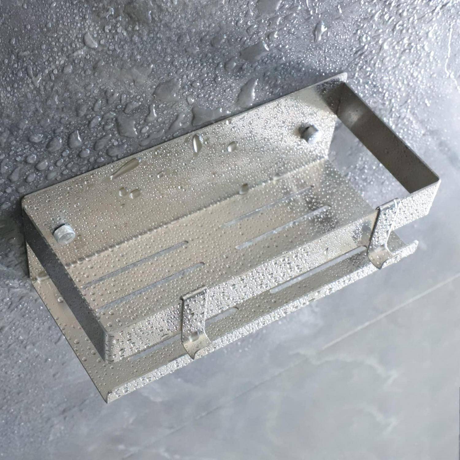 Regennass gefleckte, an der Wand montierte Metall-Ablage oder Regal mit erhöhtem Rand und zwei vorderen Haken, vor einer nassen grauen Oberfläche.