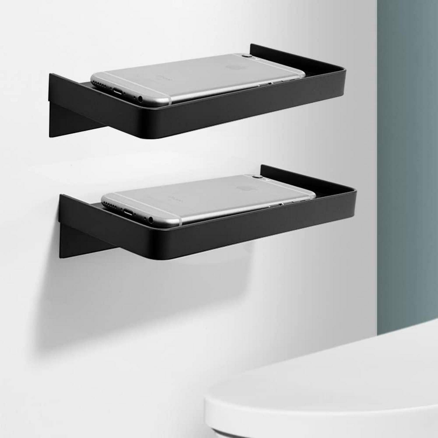 Zwei schwarze wandmontierte Regale halten silberne Smartphones und zeigen ein minimalistisches Setup zur Phonespeicherung oder zum Aufladen.