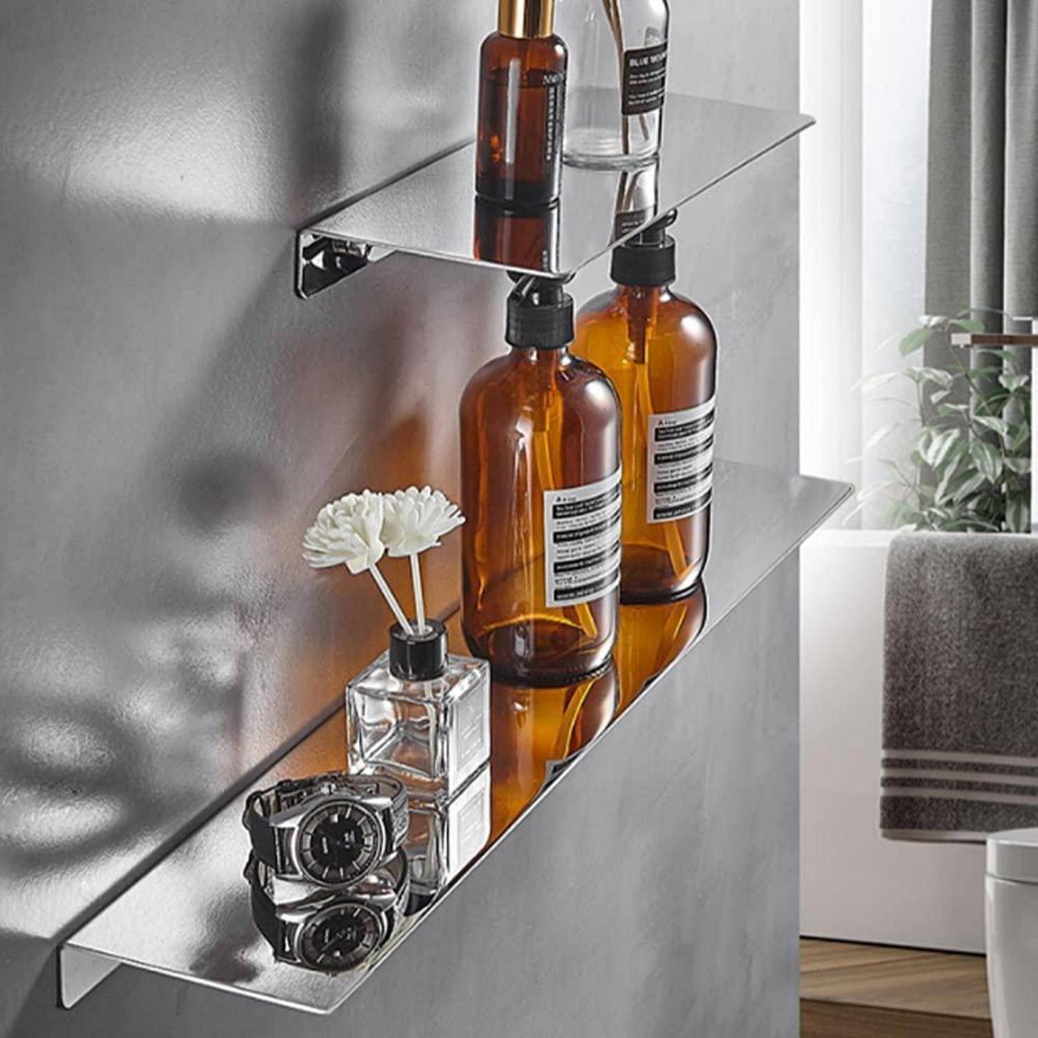 Zwei verspiegelte Wandregale halten bernsteinfarbene Flaschen, eine durchsichtige Pumpflasche, eine kleine Vase mit weißen Blüten und zwei Armbanduhren in einem modernen Zimmer.
