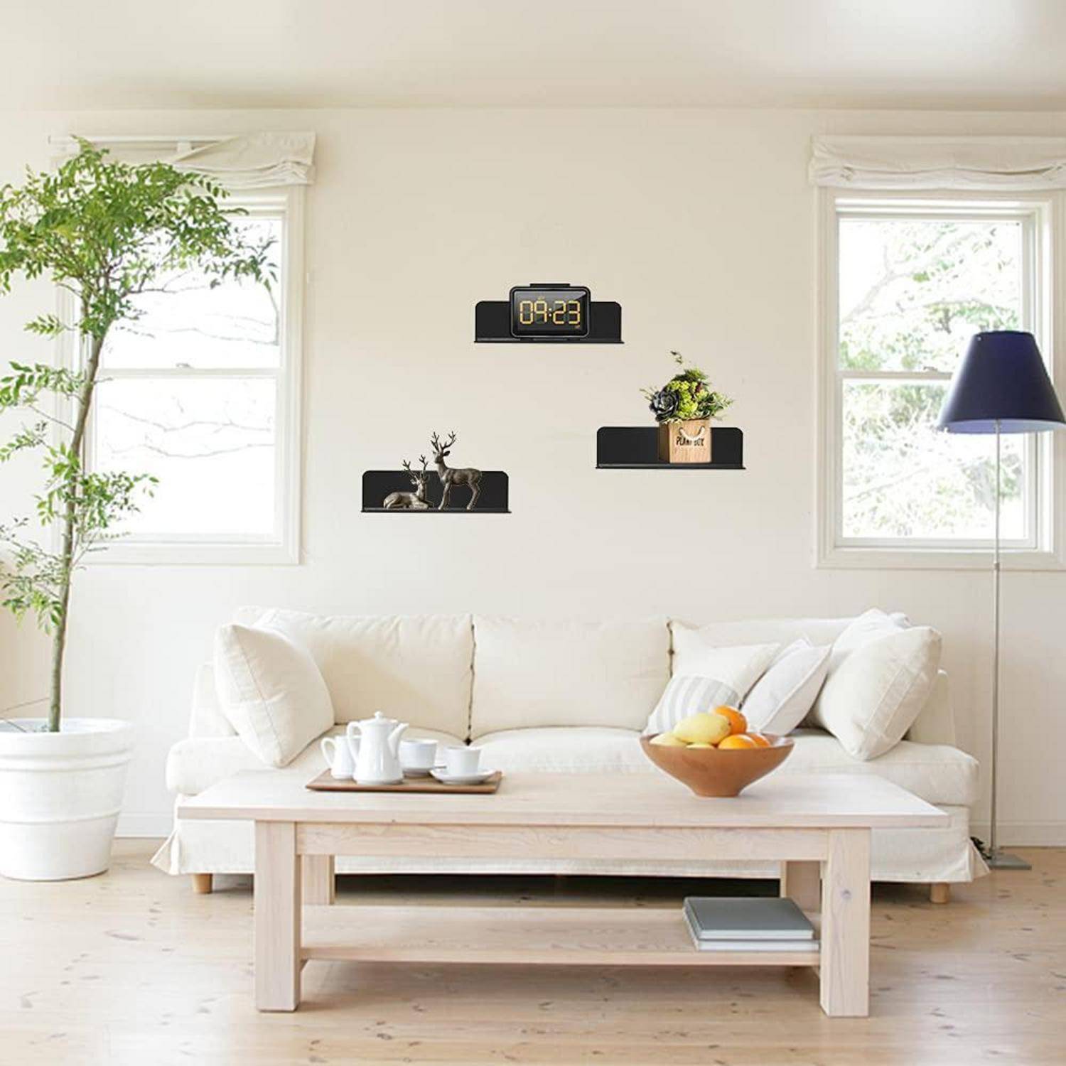 Helles minimalistisches Wohnzimmer mit weißem Sofa, Couchtisch, Topfpflanzen, Wandregalen und Digitaluhr, die 09:23 Uhr anzeigt.