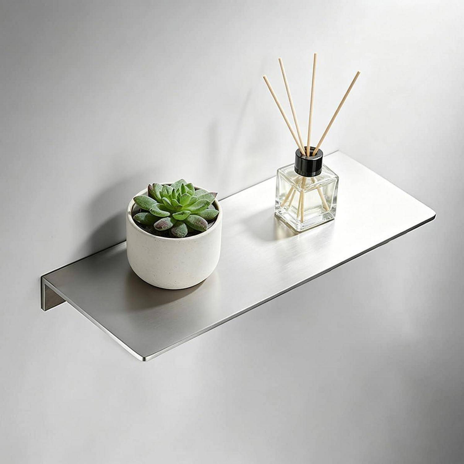Minimalistische wandmontierte Ablage mit einer Topfpflanze eines Sukkulenten und einem Glaszerstäuber mit Duftstäbchen vor einer einfachen, hellen Wand.