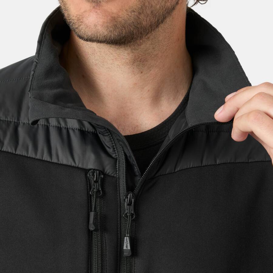 Nahaufnahme eines Mannes, der eine schwarze Jacke mit Reißverschluss trägt, mit offenem Kragen und seiner Hand, die die vordere Kante hält.