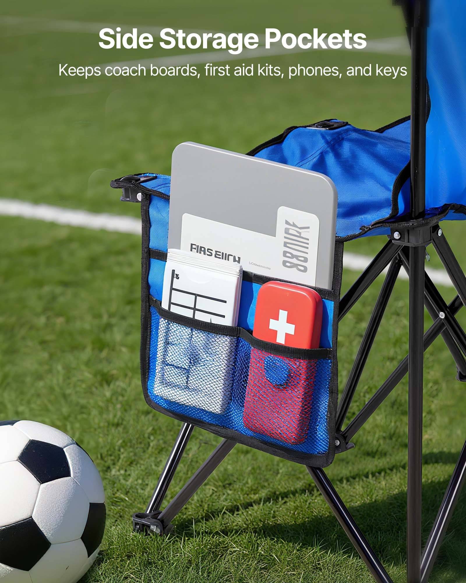 Blauer Klappstuhl mit Seitentaschen, auf dem ein Trainertafel, ein Erste-Hilfe-Kasten, ein Telefon und Schlüssel liegen, auf einem Fußballplatz, mit einem Fußball in der Nähe.