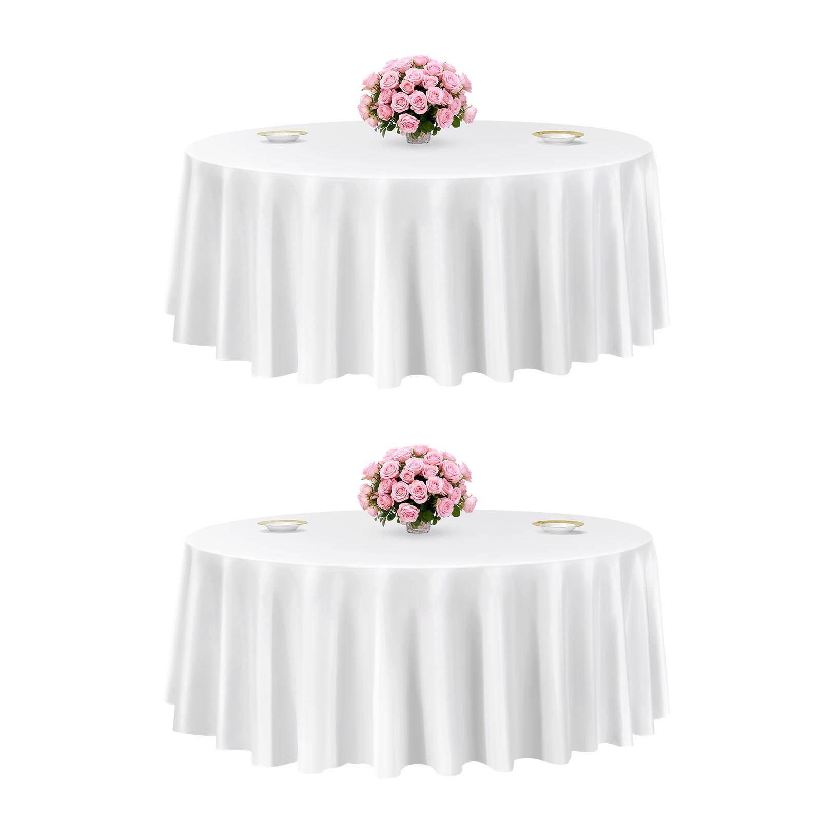 Zwei runde Tische mit weißen Tischdecken und rosa Blumengestecken als Mittelpunkte, jeweils mit kleinen Tellern auf einem schlichten weißen Hintergrund eingedeckt.