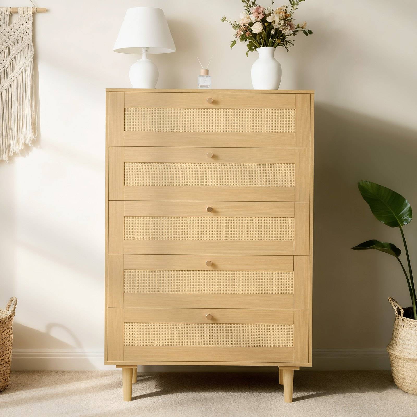 Helles Holz-Kommode mit fünf Schubladen und geflochtenen Frontpaneelen, oben gekrönt mit einer Lampe, einer Blumenvase und kleinen Dekorationselementen in einem hellen Schlafzimmer.