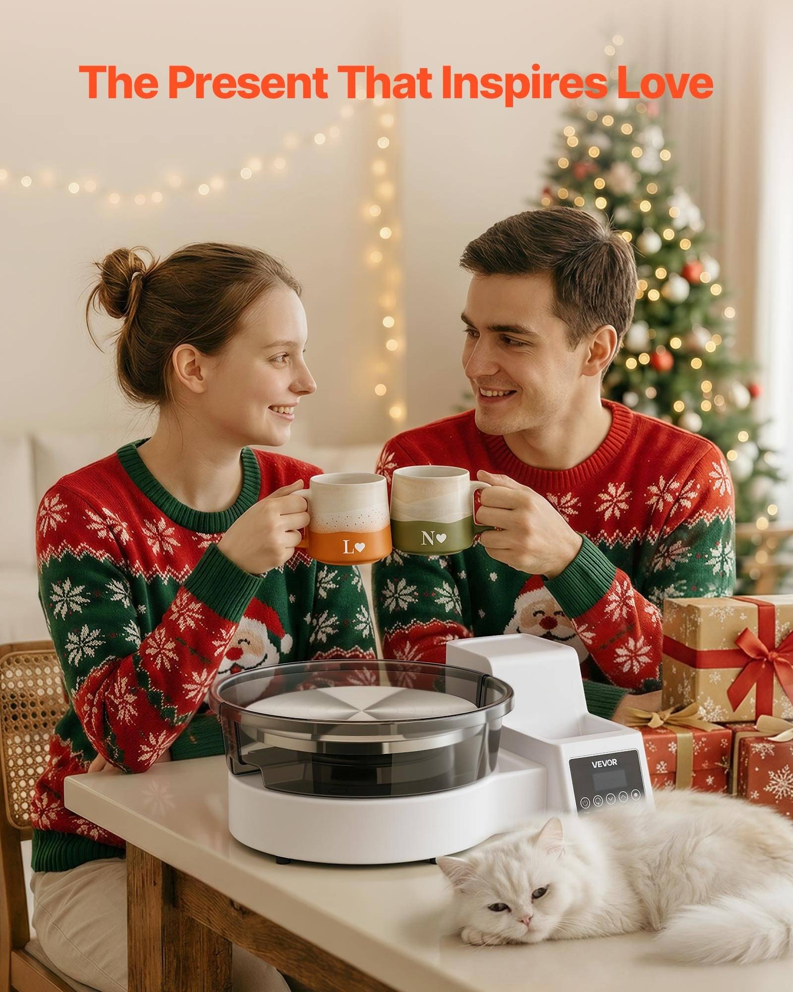 Lachendes Paar in passenden Weihnachtspullovern stoßt mit Tassen neben einem weißen Roboterstaubsauger und einer schlafenden Katze an, mit einem geschmücktem Weihnachtsbaum und Geschenken hinter ihnen.